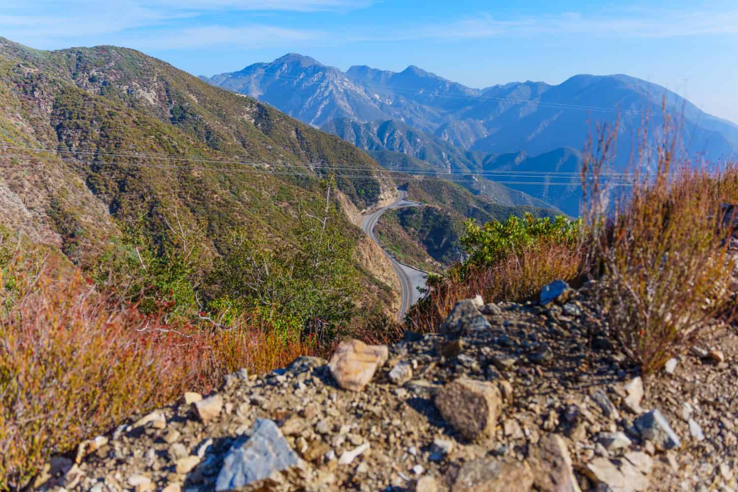 Scenic view of a winding road through mountainous terrain in California, framed by vibrant vegetation and rocky formations, ideal for outdoor enthusiasts.