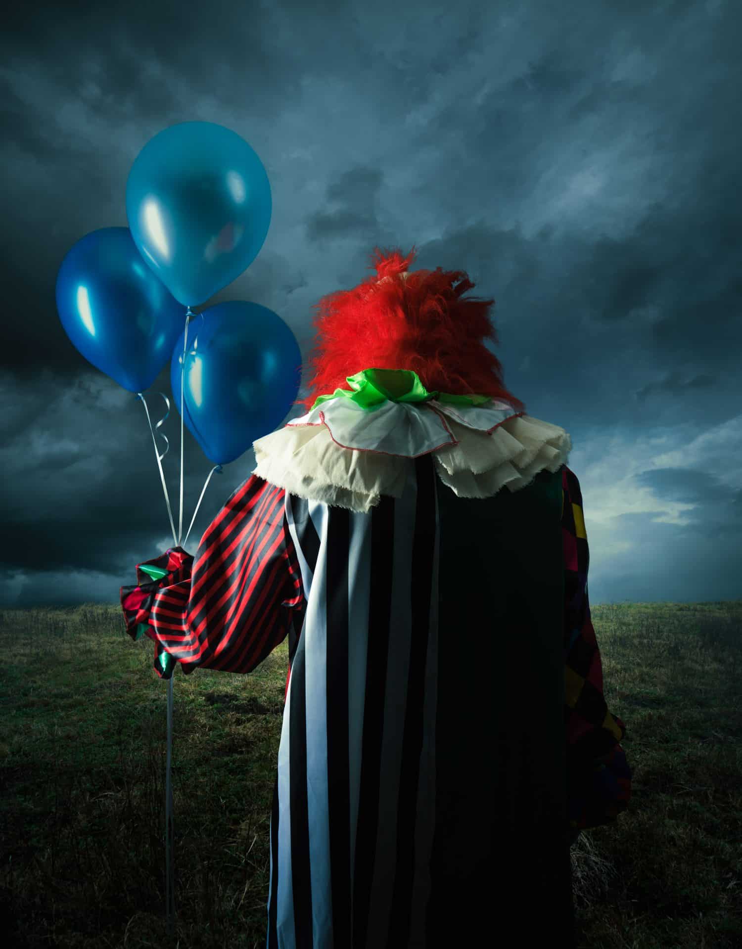 High contrast image of a scary clown with blue balloons on a field