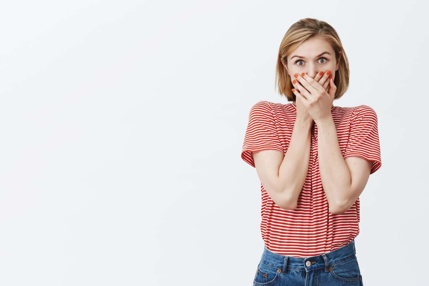 Girl trying to hide secret, wanting to tell everyone, being talkative. Excited over-emotive european female student in striped t-shirt, covering mouth with palms not to say word, shocked and intense