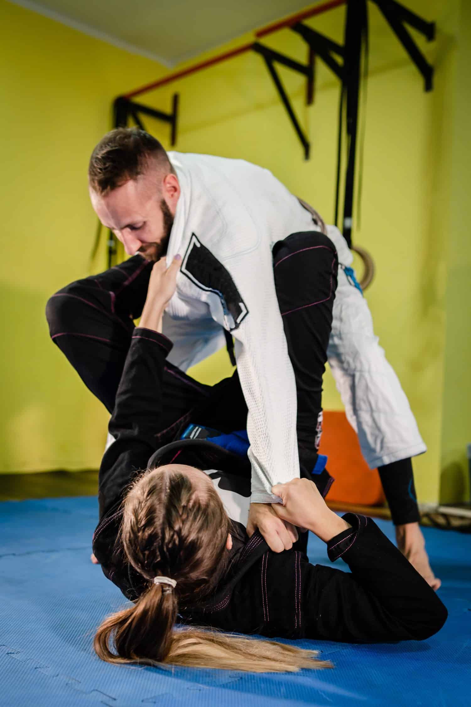 Young bjj couple man and woman male and female girl training martial arts brazilian jiu jitsu jiujitsu at the academy wearing black white kimono gi guard holding collar and sleeve