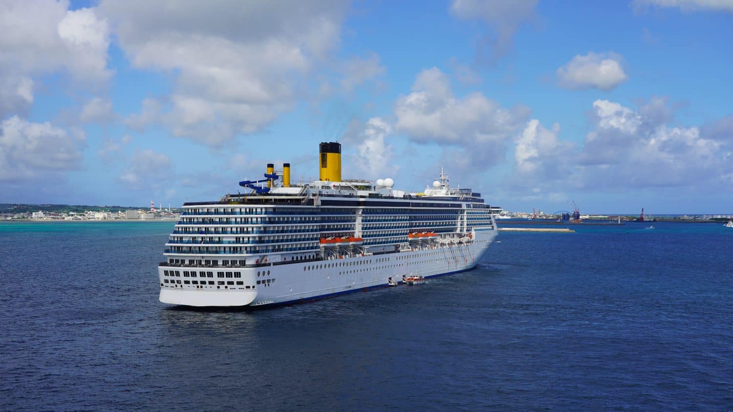 large white cruise ship anchored off the coast of a tropical island in japan in turquoise blue ocean water on background blue sky clouds. cruise vessel in Pacific Ocean. safety boats with liner