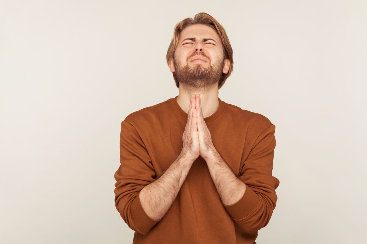 Sincere request to god. Portrait of imploring man with beard in sweatshirt praying up heartily, feeling guilty, pleading begging help from heaven. indoor studio shot isolated on gray background