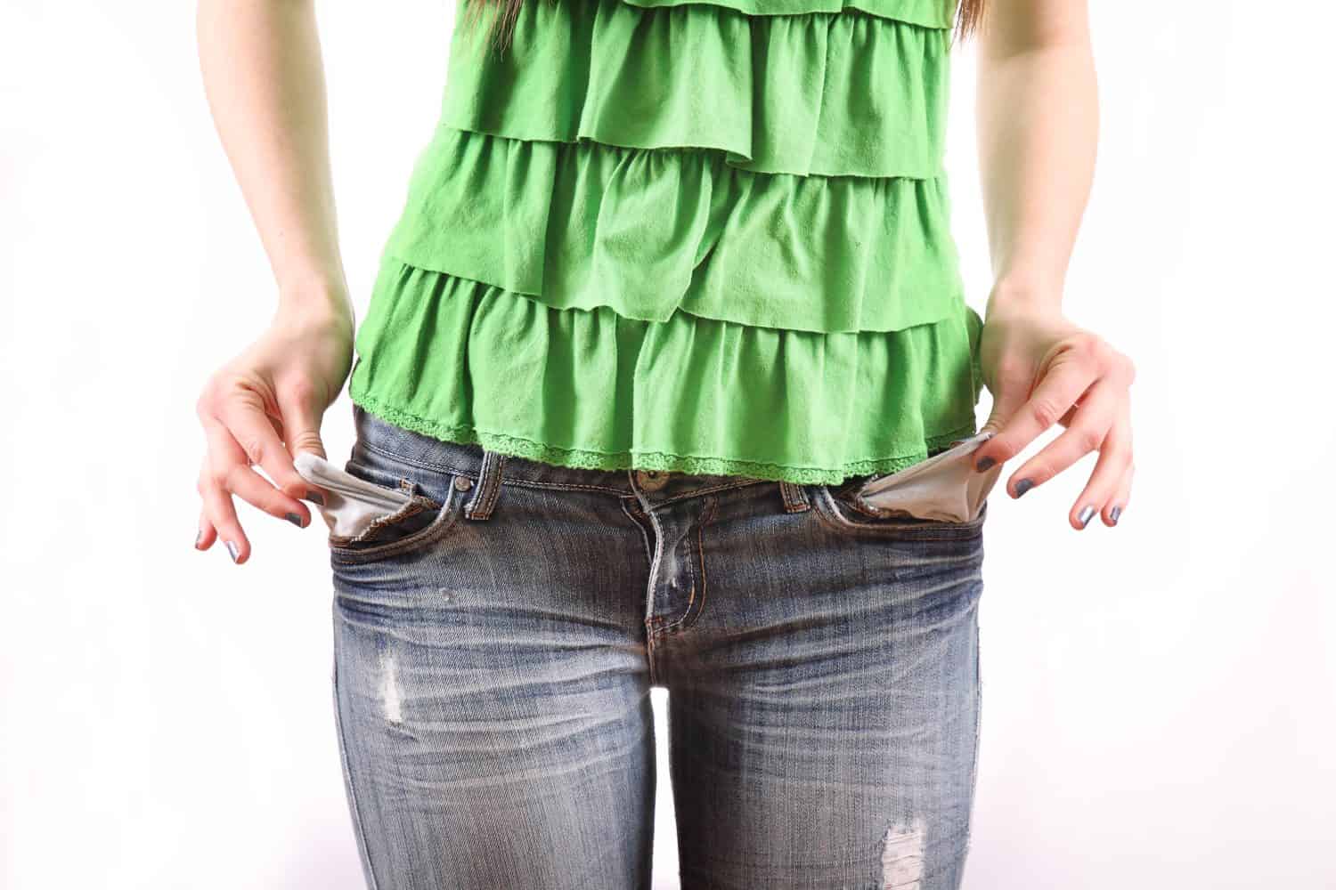 thin female broke college student pulling out pockets to reveal no money isolated on white