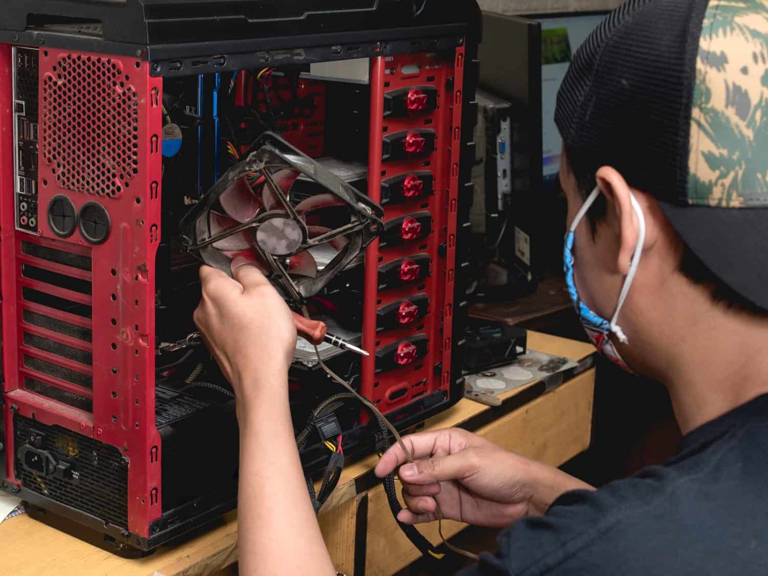 A computer technician disconnects and removes an old, dirty and defective cooling fan from a desktop computer. IT support or DIY repair concept.