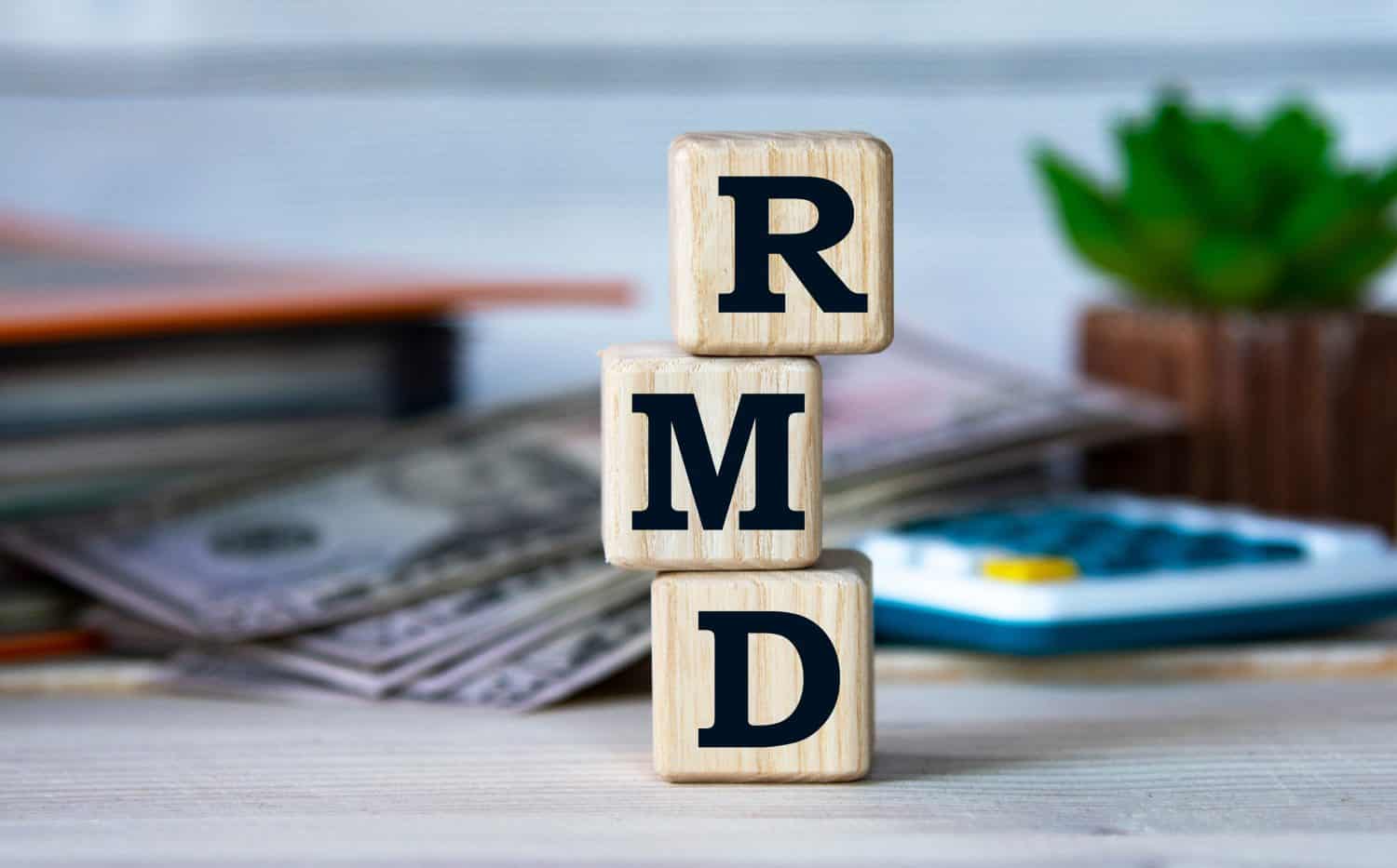 RMD (Required Minimum Distribution) - Abbreviation for wooden cubes on the background of a folder, cactus and banknotes. Business concept