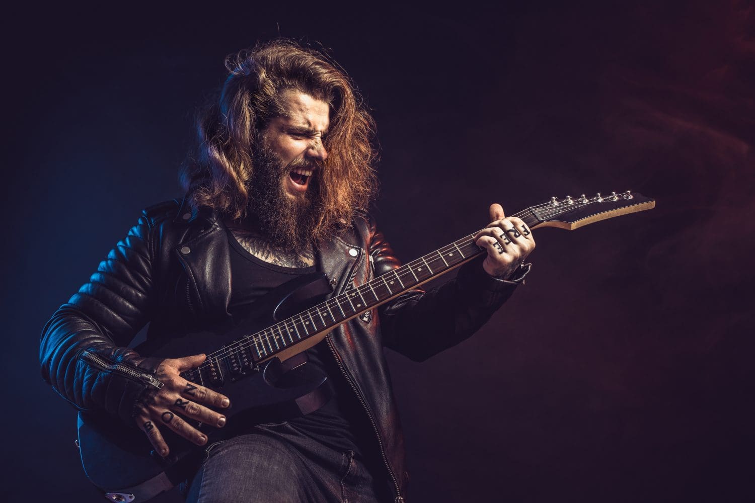 Guitar player. Rockstar bearded man with long hair emotional plays on guitar isolated on black background. Studio shot