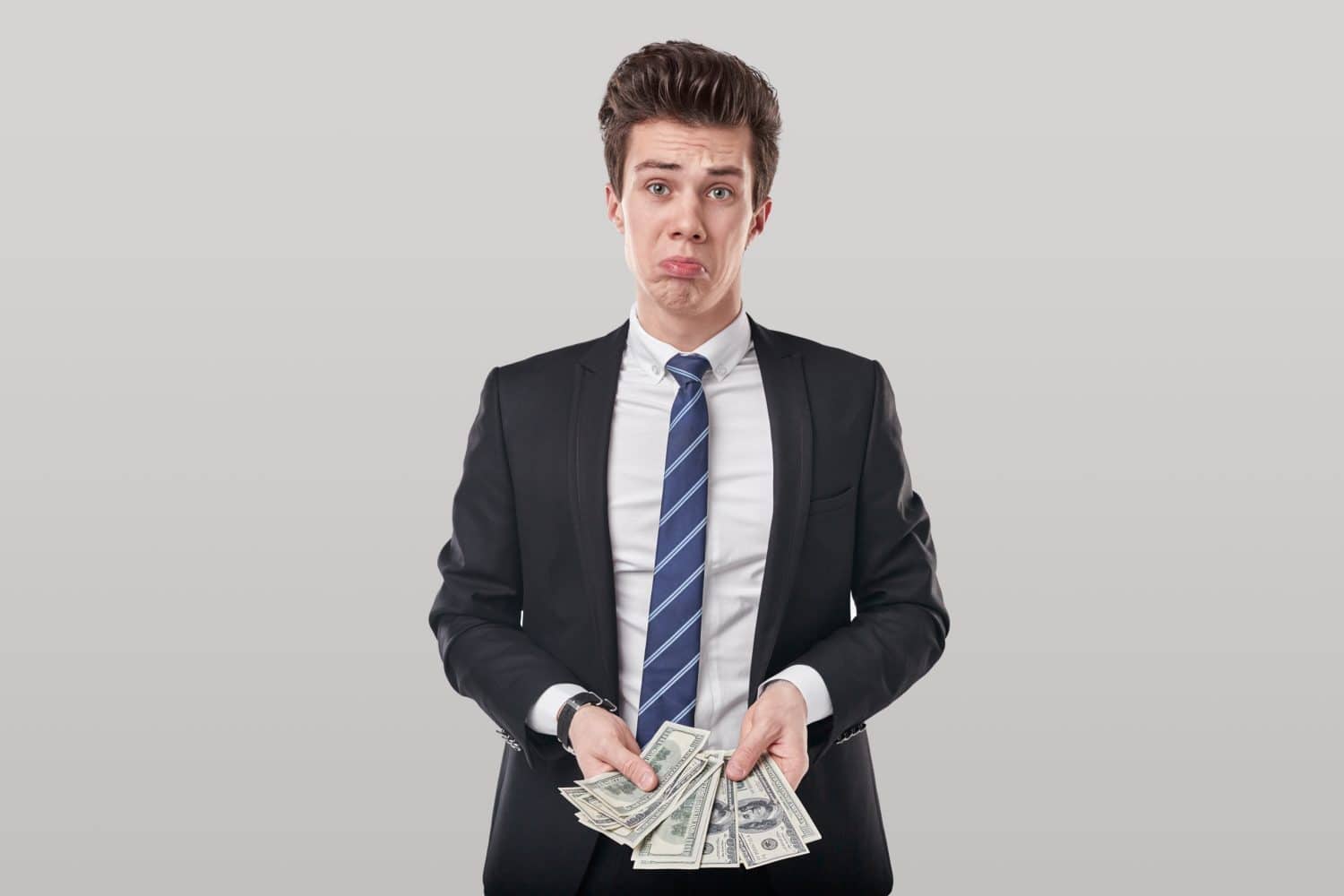 Sad male entrepreneur with lack of money making funny face and standing on gray background in studio