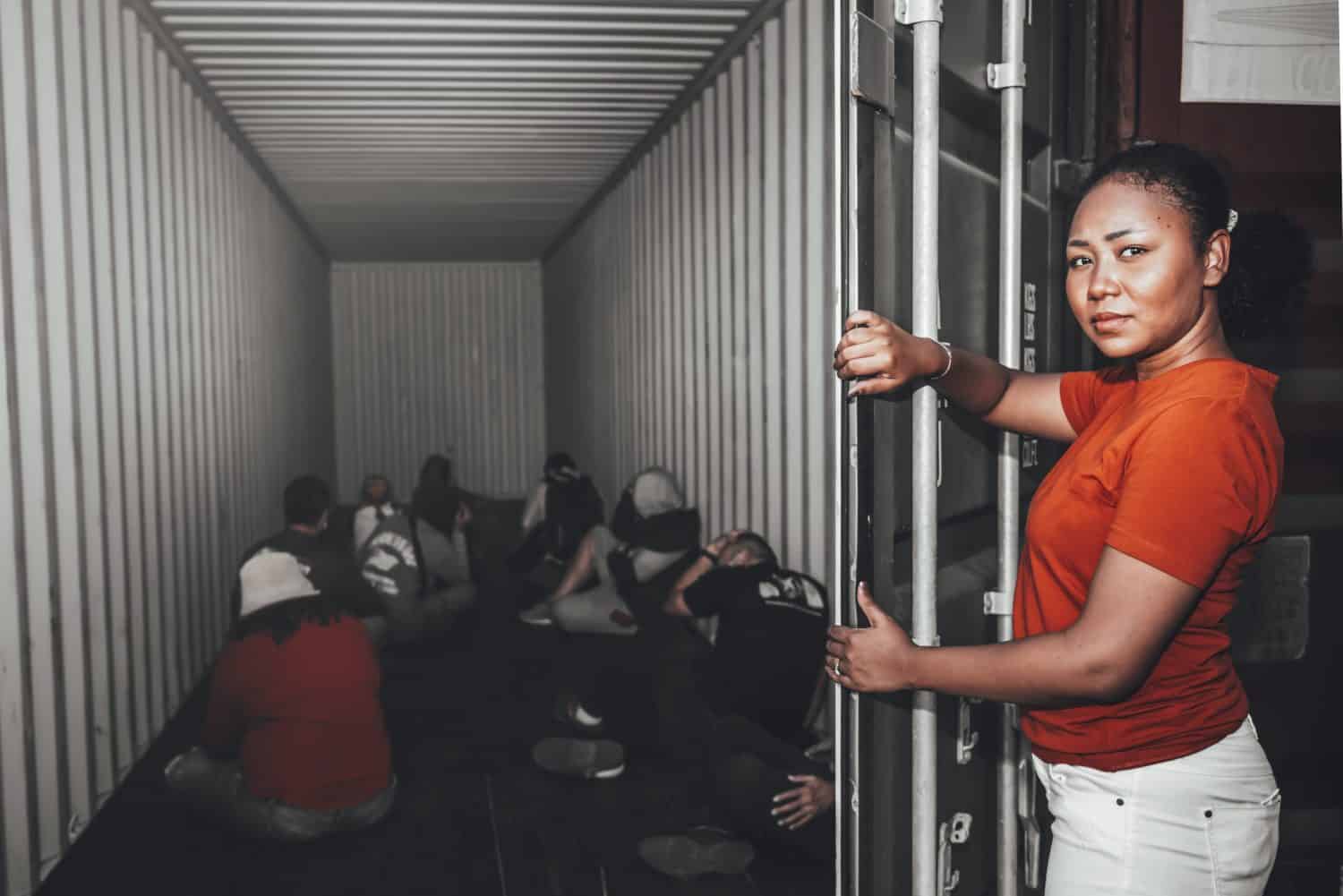 An African women Opening the door of a container, inside of which serveral people were sitting, to human trafficking and illegal immigration concept.