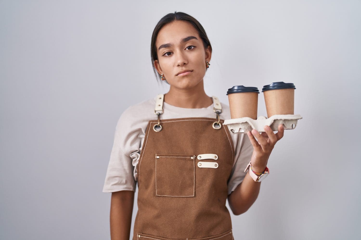 Young hispanic woman wearing professional waitress apron holding coffee looking sleepy and tired, exhausted for fatigue and hangover, lazy eyes in the morning.