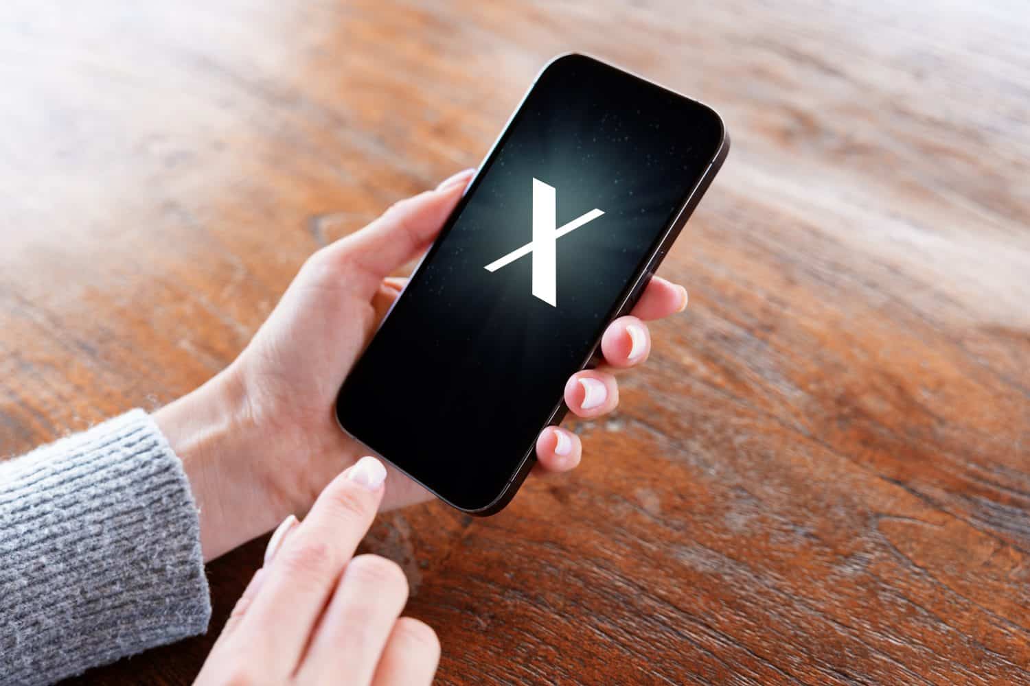 Person holding mobile phone with a letter X on the screen