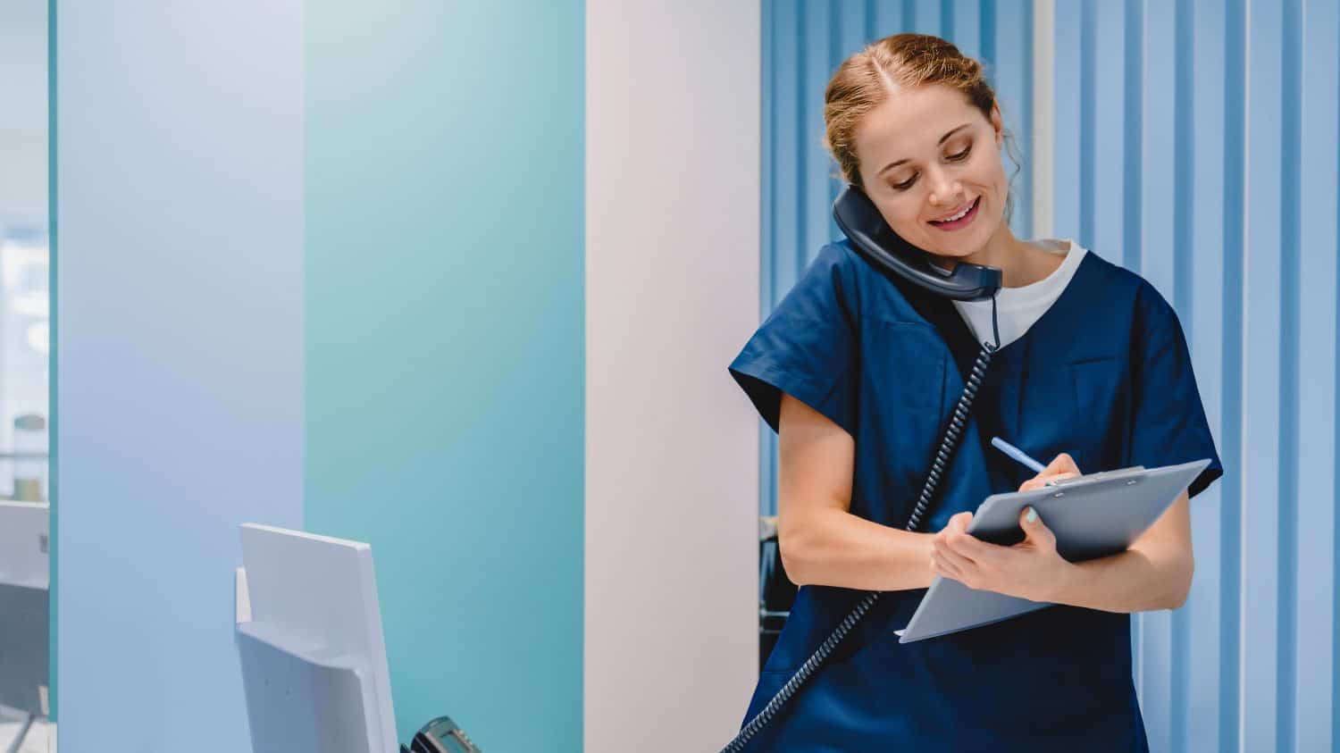 Caucasian female practitioner working at reception desk while answering phone calls and scheduling appointments in medical clinic. Hospital concept.