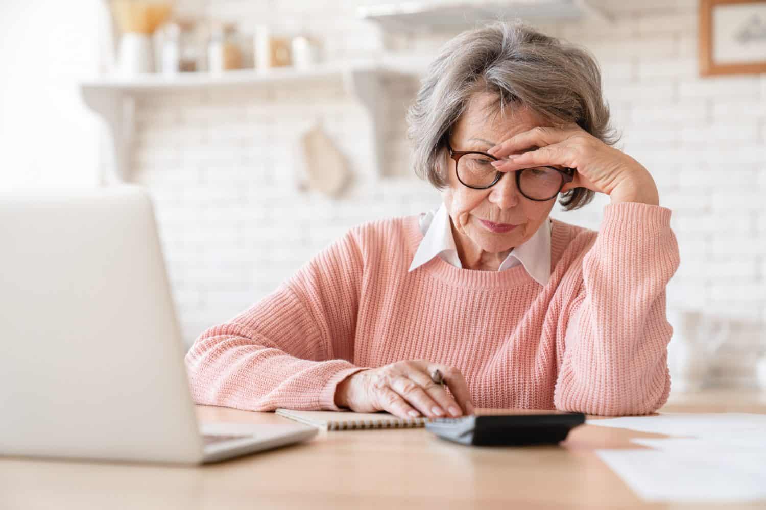 Trouble and problems with money. Old elderly senior grandmother woman using laptop calculator for counting funds pension paying domestic bills, loan mortgage, health insurance