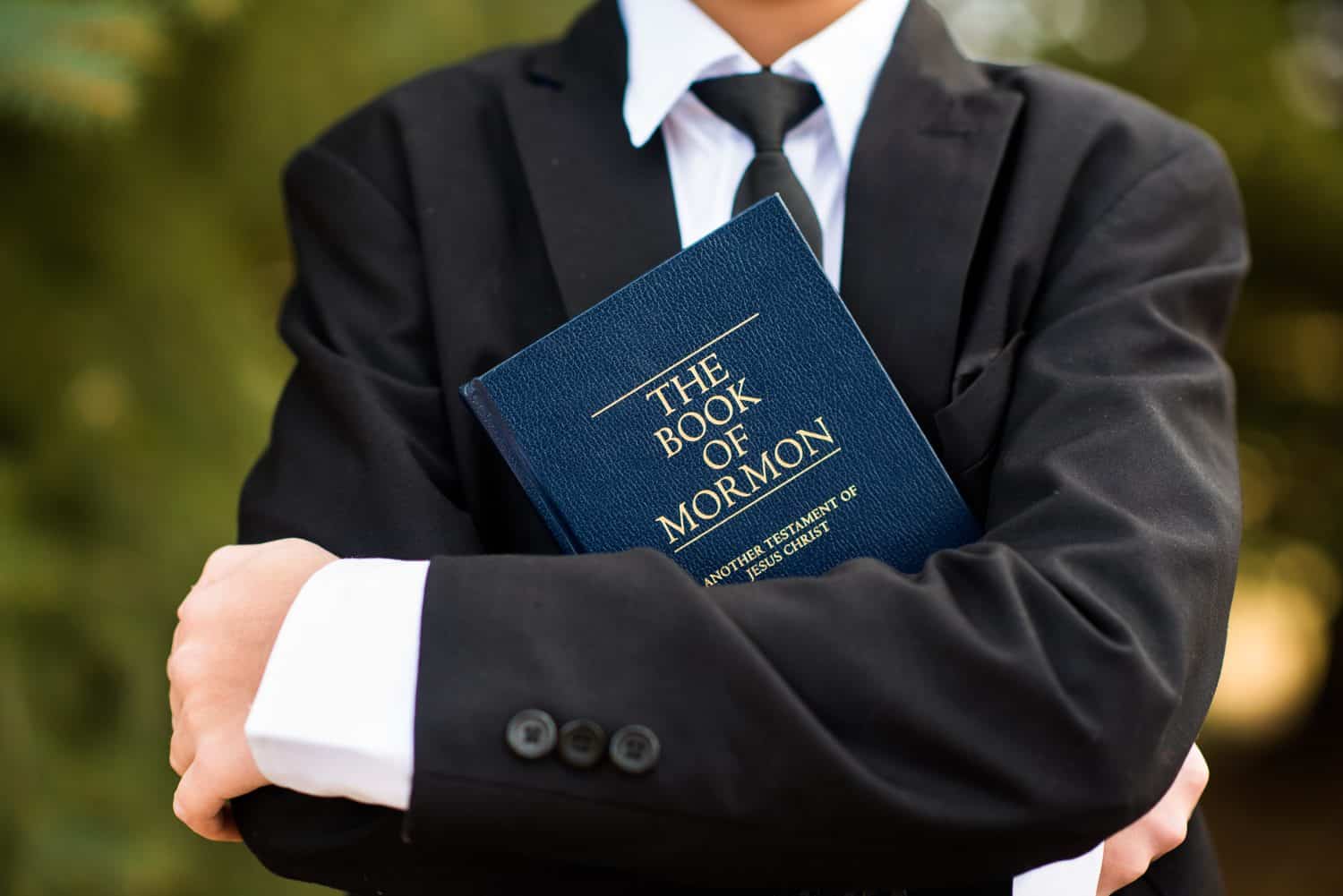 Closeup of the arms of a young boy with his arms folded around the Book of Mormon. Boy in suit and tie.