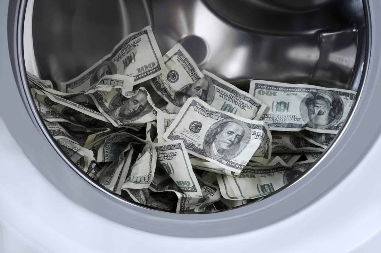 Many a hundred dollar bills inside the drum of a washing machine. American paper money in the washing machine. Conceptual image of criminal money laundering.