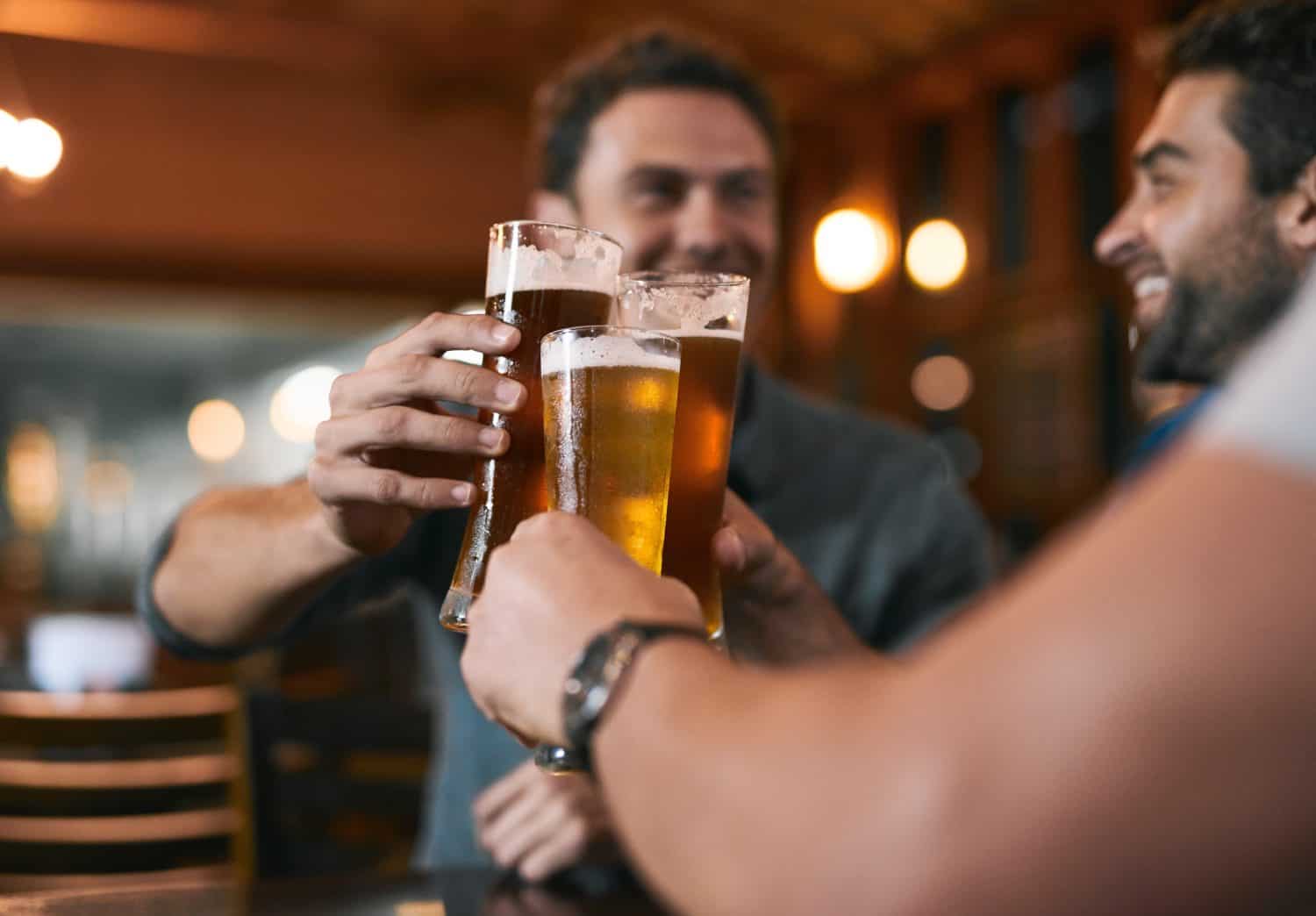 Cheers, friends and beer in pub with glasses as celebration for drinks, happiness or social bonding. Alcohol, men and people in restaurant for birthday party, event and reunion in Germany with toast