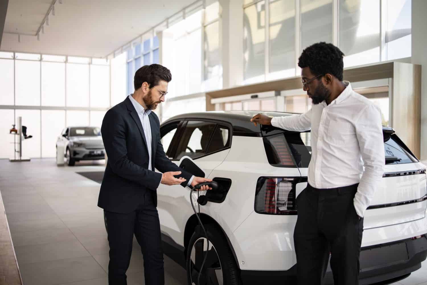 Dealer sells electric SUV to businessman in modern car dealership. Business negotiation about environmentally-friendly vehicle. Modern showroom conveys professional atmosphere.