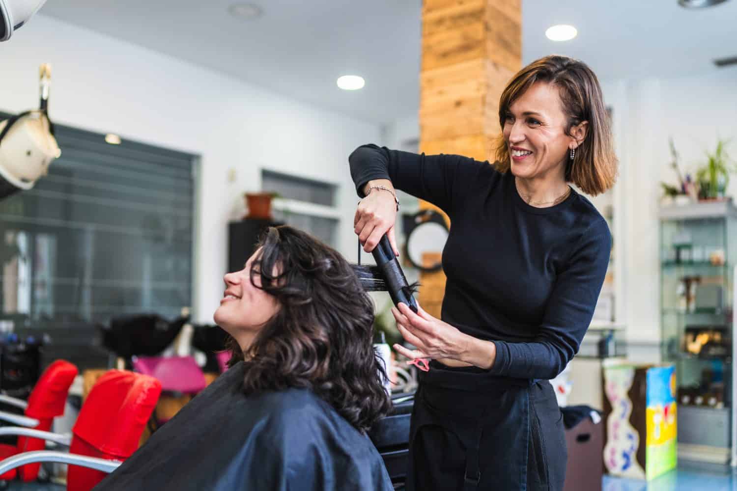 A hairdresser uses a curling iron to curl a client&#039;s hair in a modern salon. The setting is professional and stylish. Concept of professional hair curling.