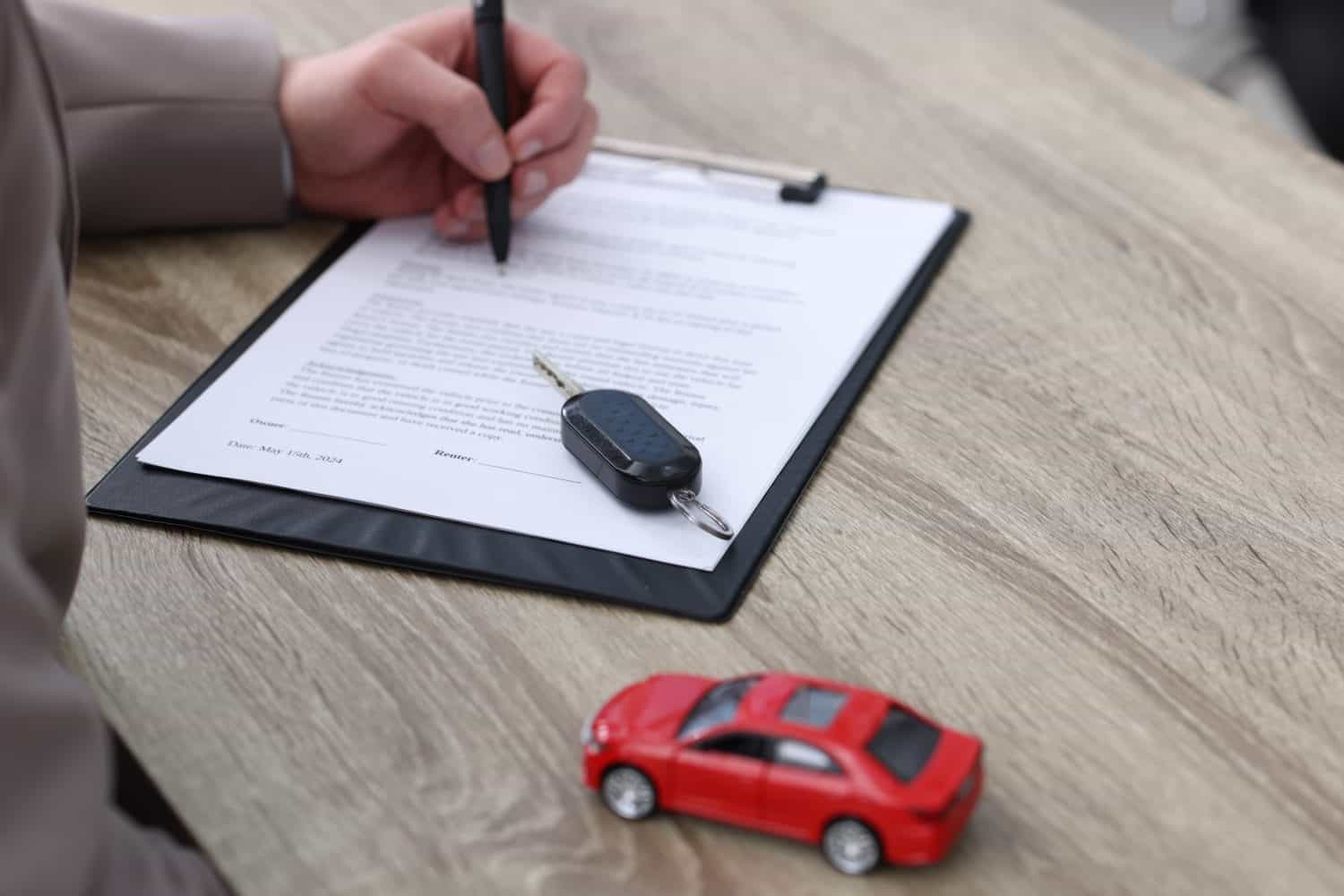 Man signing car purchase agreement at wooden table, selective focus. Buying auto