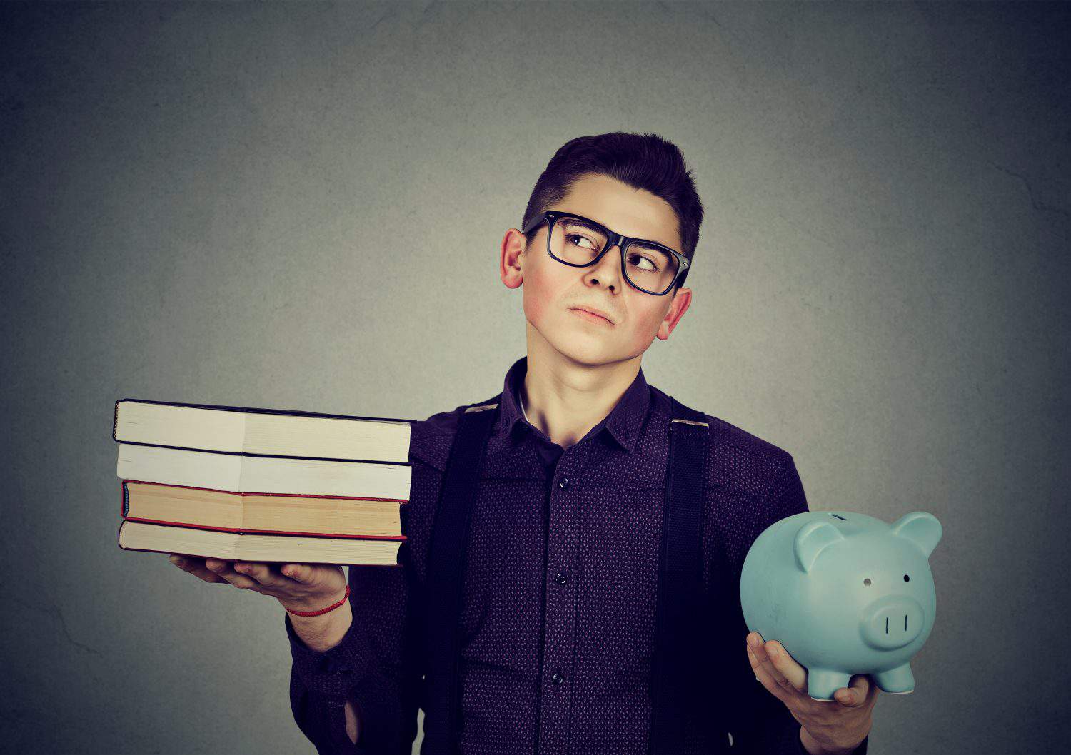 Student loan concept. Young man with stack pile of books and piggy bank full of debt rethinking future career path