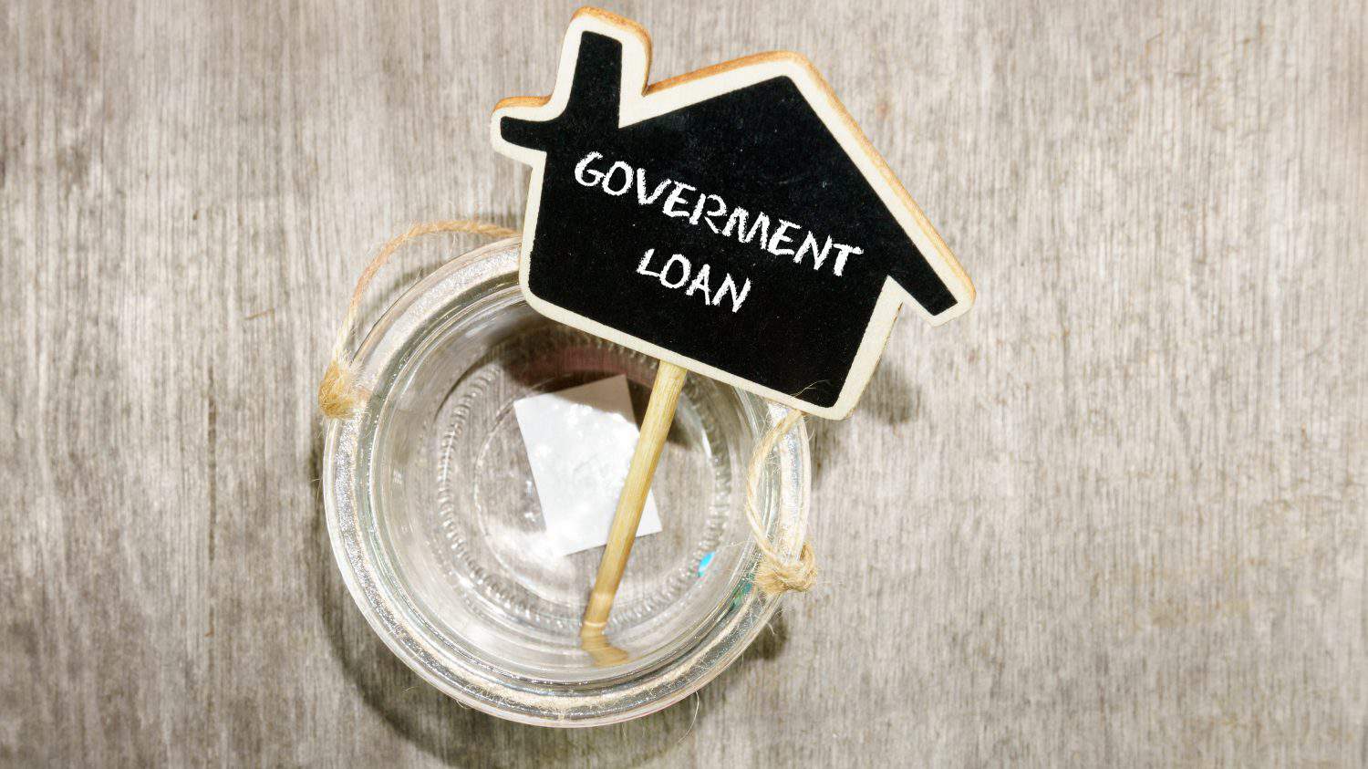 Word Government Loan on mini chalkboard with empty jar on wooden base