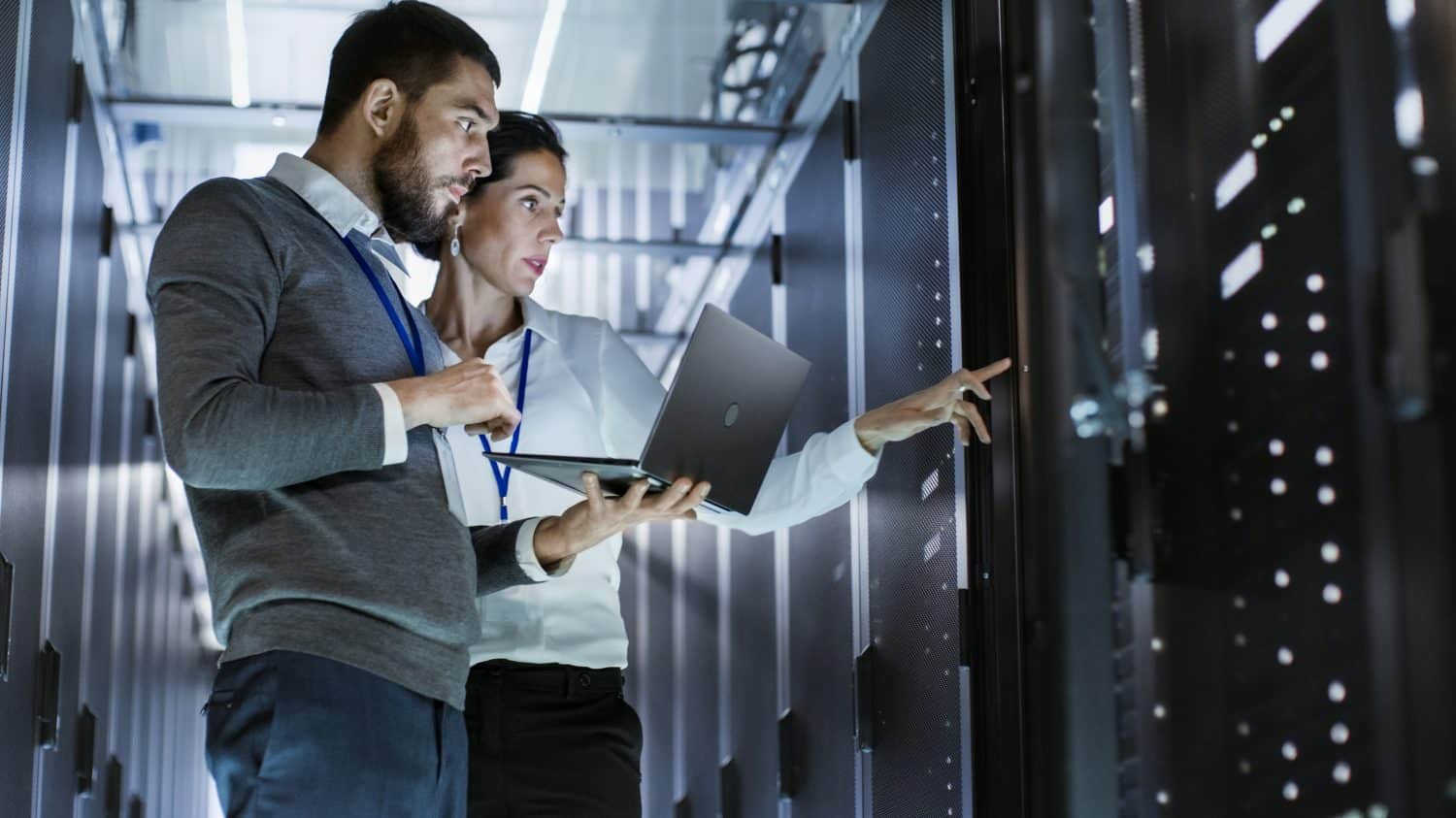 Male IT Specialist Holds Laptop and Discusses Work with Female Server Technician. They&#039;re Standing in Data Center, Rack Server Cabinet is Open.