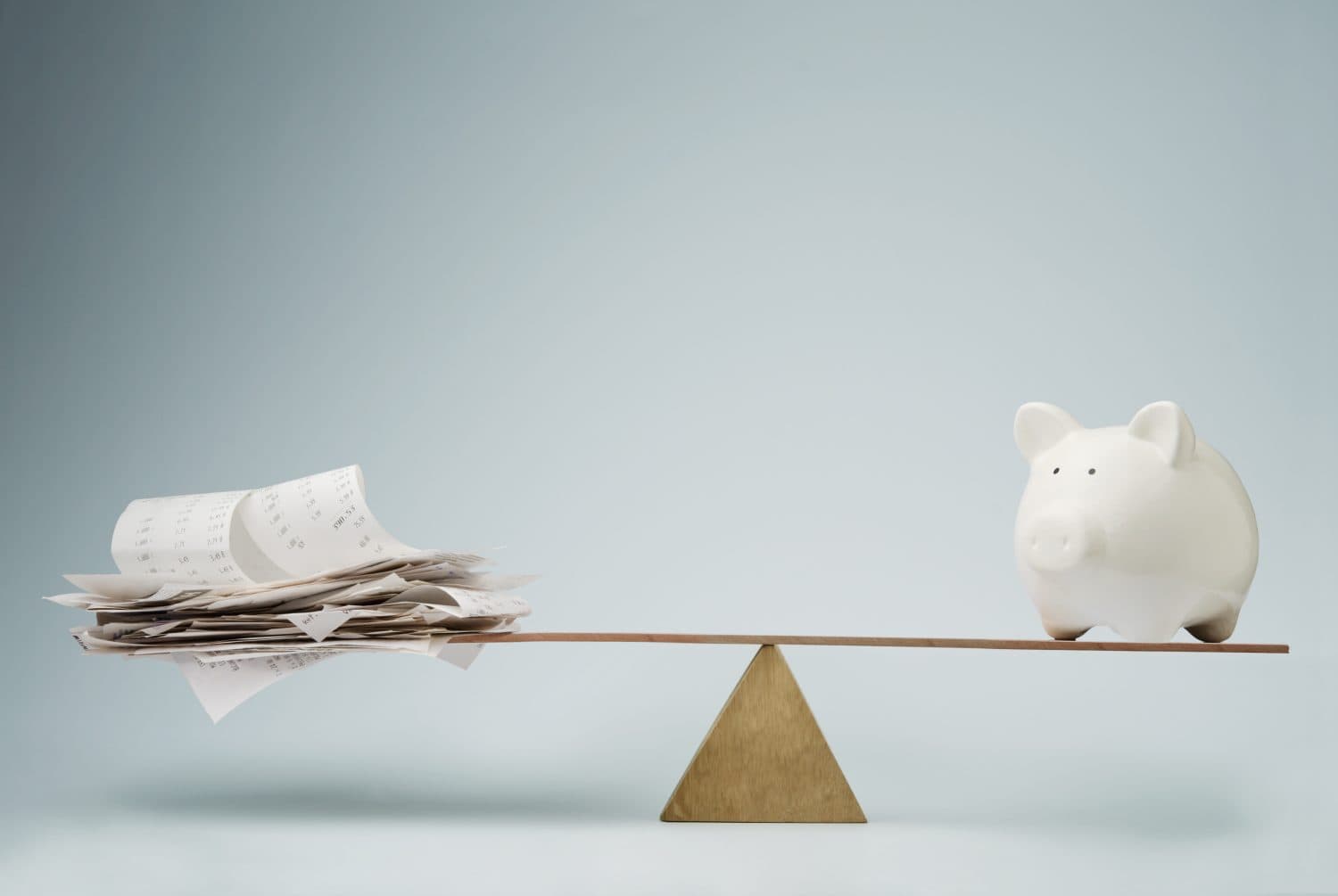 Piggy bank balancing on seesaw over a stack of bills