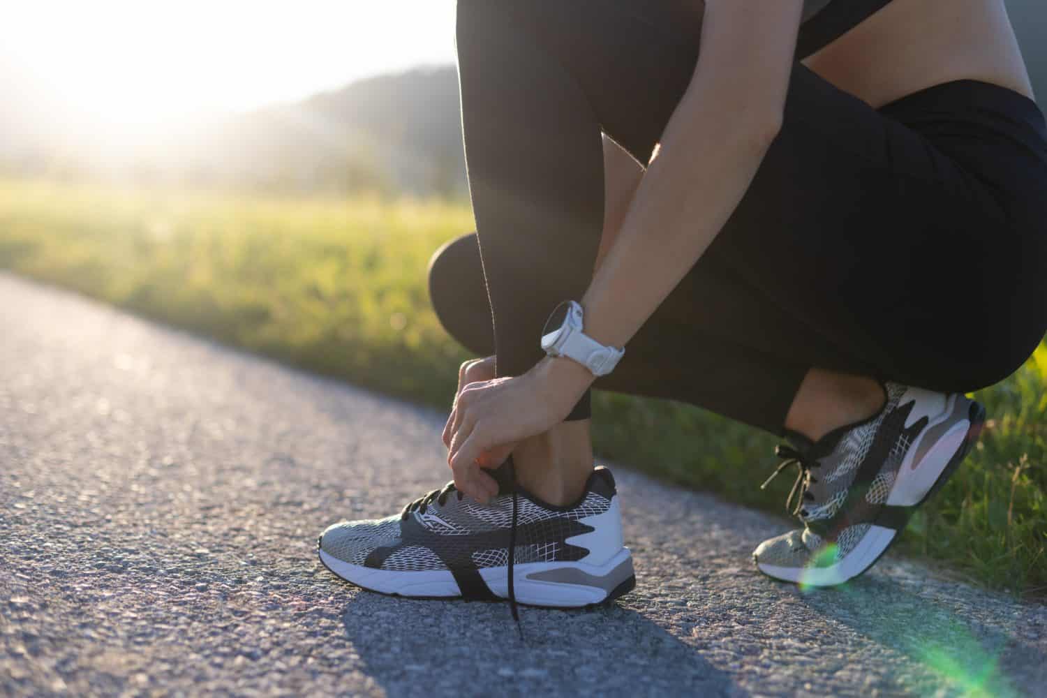 Low section of a young woman tying her running shoes before training