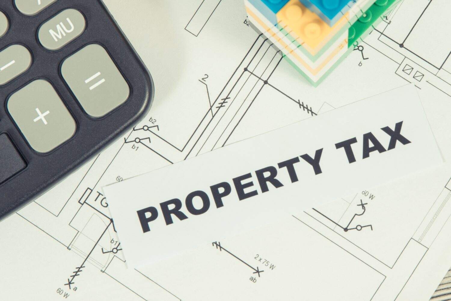 Inscription property tax with small house made of colorful toy blocks and calculator. Increasing real estate or luxury taxation. Tax payments