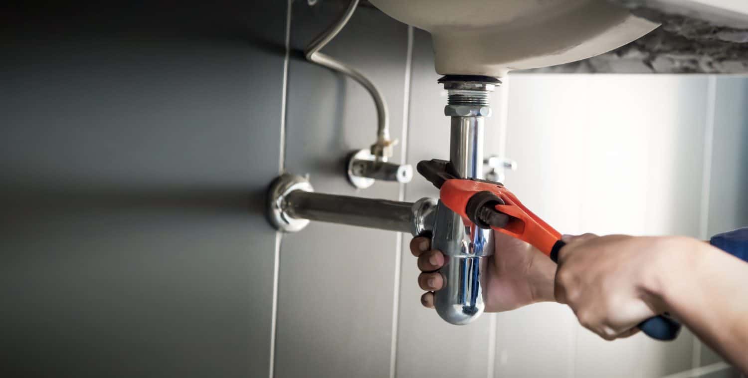 Plumber uses wrench to repair water pipe under sink There is maintenance to fix the water leak in the bathroom.with red wrench, plumbing install concept.
