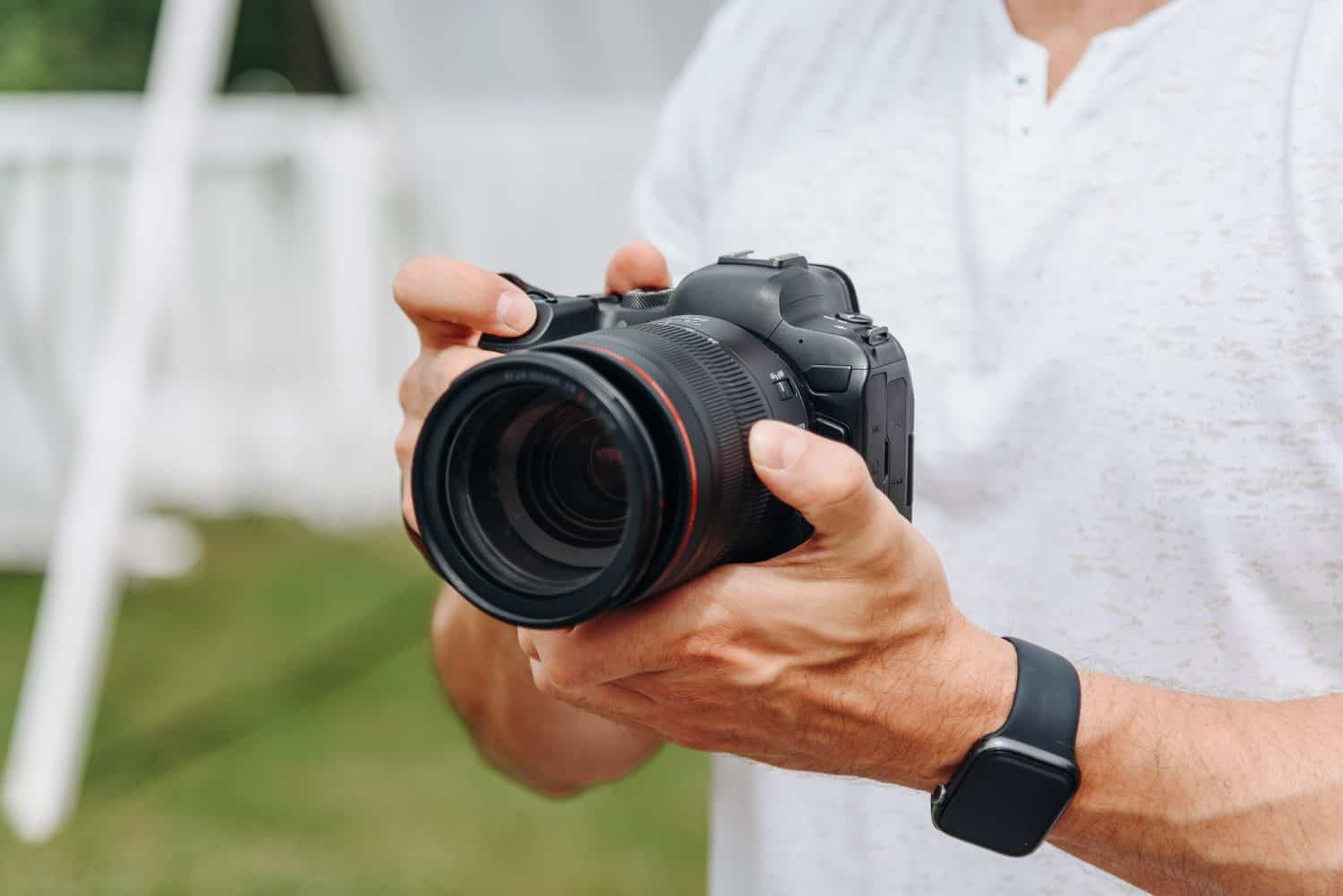 dslr camera in hands, young adult caucasian photographer in white t-shirt at work outdoors in sunny summer day