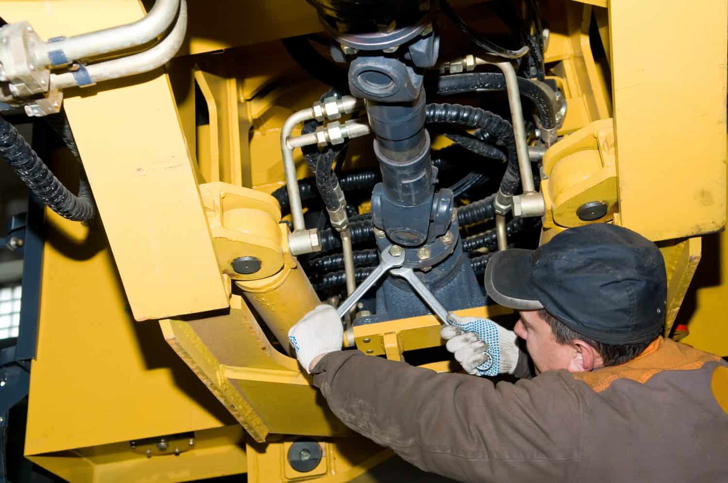 repairman worker screwing nuts of axle assembly in heavy wheel loader