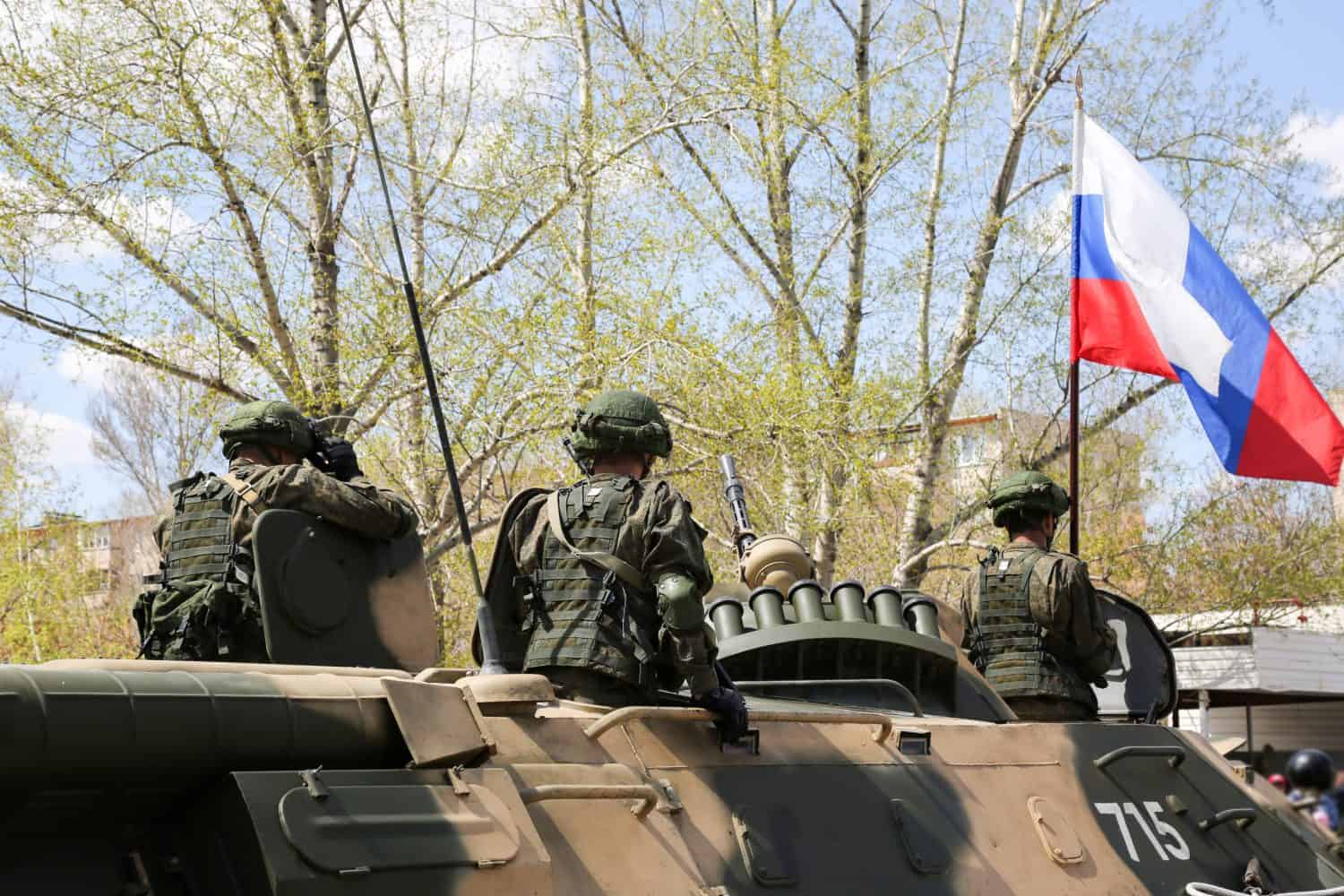 The soldiers are standing in the open hatches of the tank. The Russian military on military equipment is going around the city.