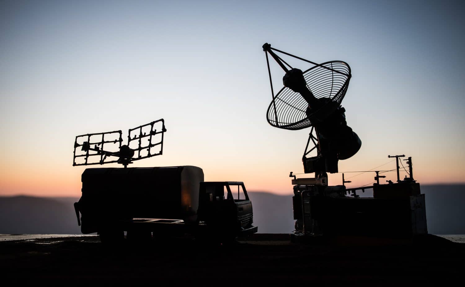 Creative artwork decoration. Silhouette of mobile air defence truck with radar antenna during sunset. Satellite dishes or radio antennas against evening sky. Selective focus