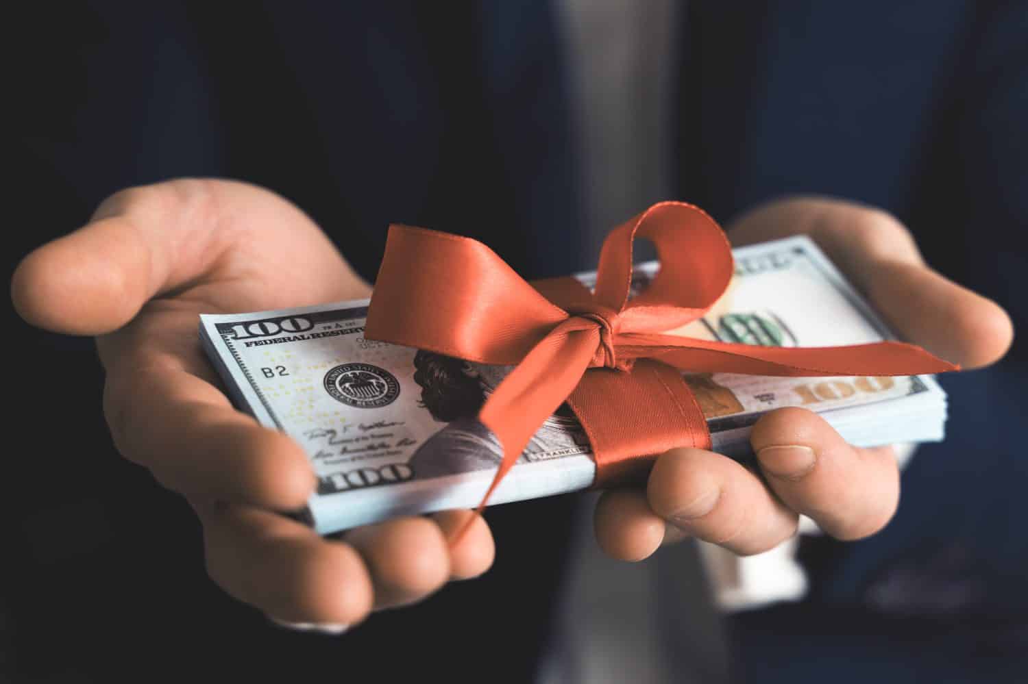 Concept, money as a gift, win or bonus. businessman takes or gives pile of 100 dollar bills tied with red ribbon with bow.