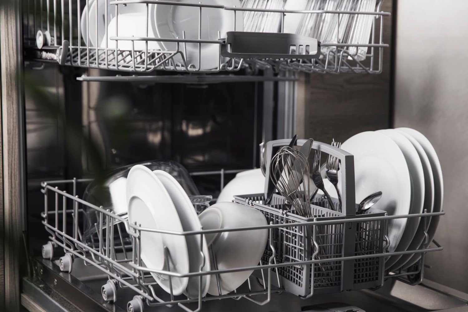 Front view of open automatic stainless steel built-in fully integrated top control dishwasher range machine with clean utensils, cutlery, glasses, dishes, plates inside in modern home kitchen