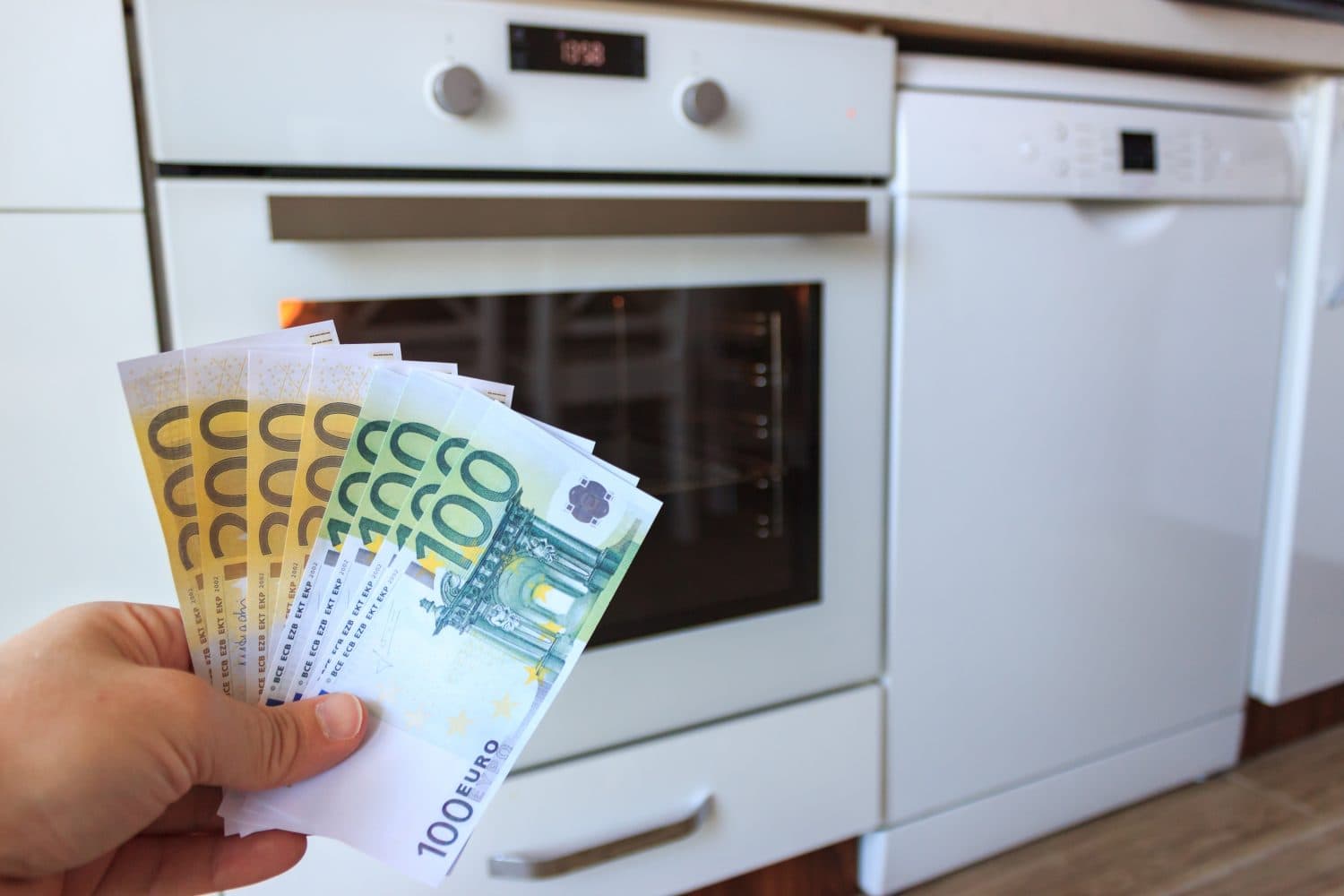 Man is holding money in his hands near the oven and dishwasher. Increase in the price of electricity. Energy crisis in Europe.