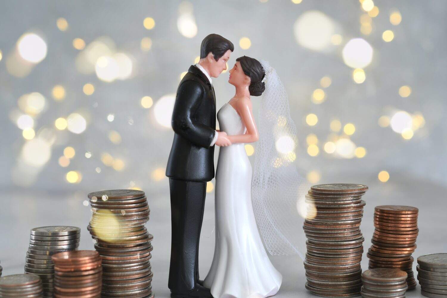 Wedding expenses concept - bride and groom with stacks of coin money