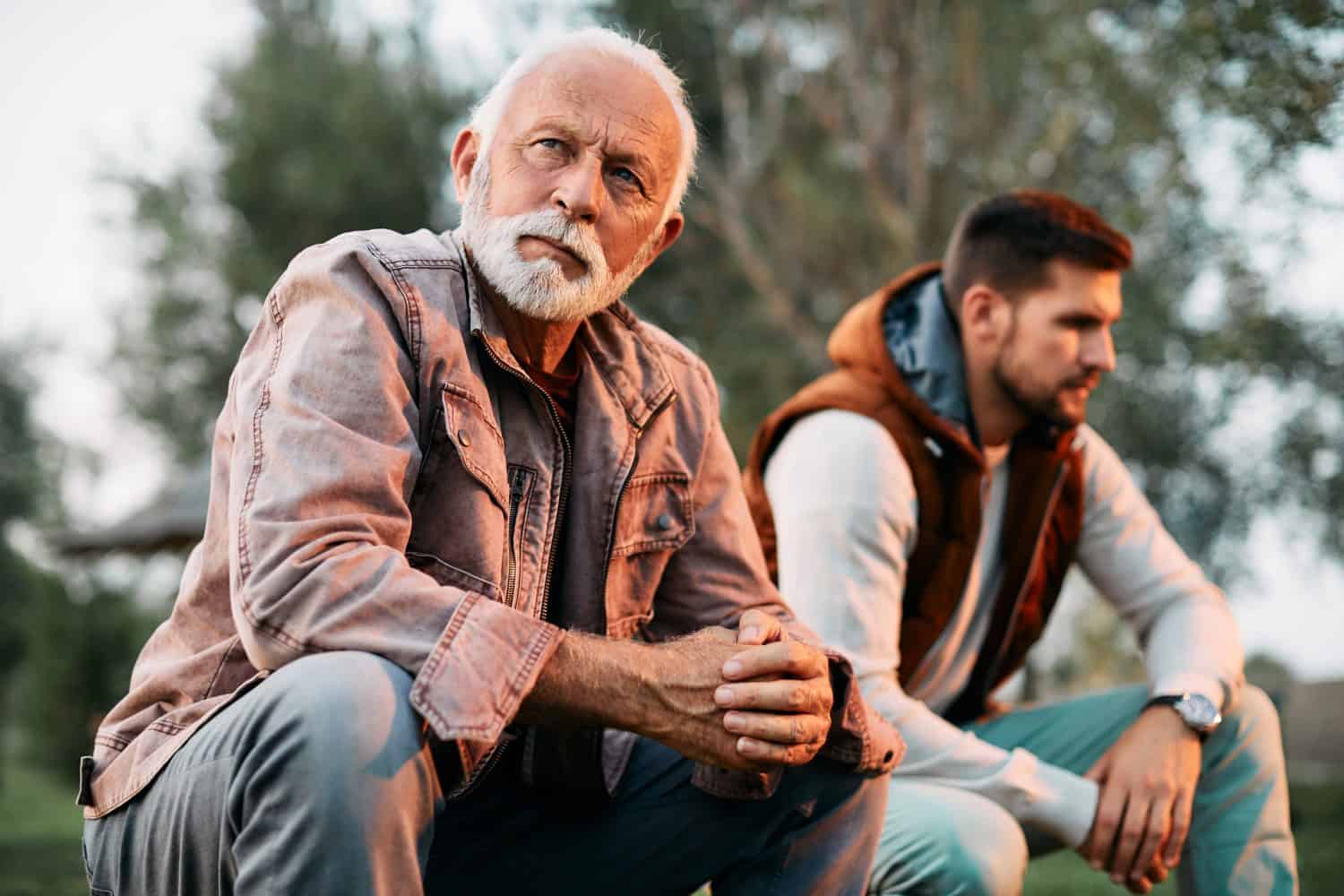Pensive senior father ignoring his adult son after an argument in nature.