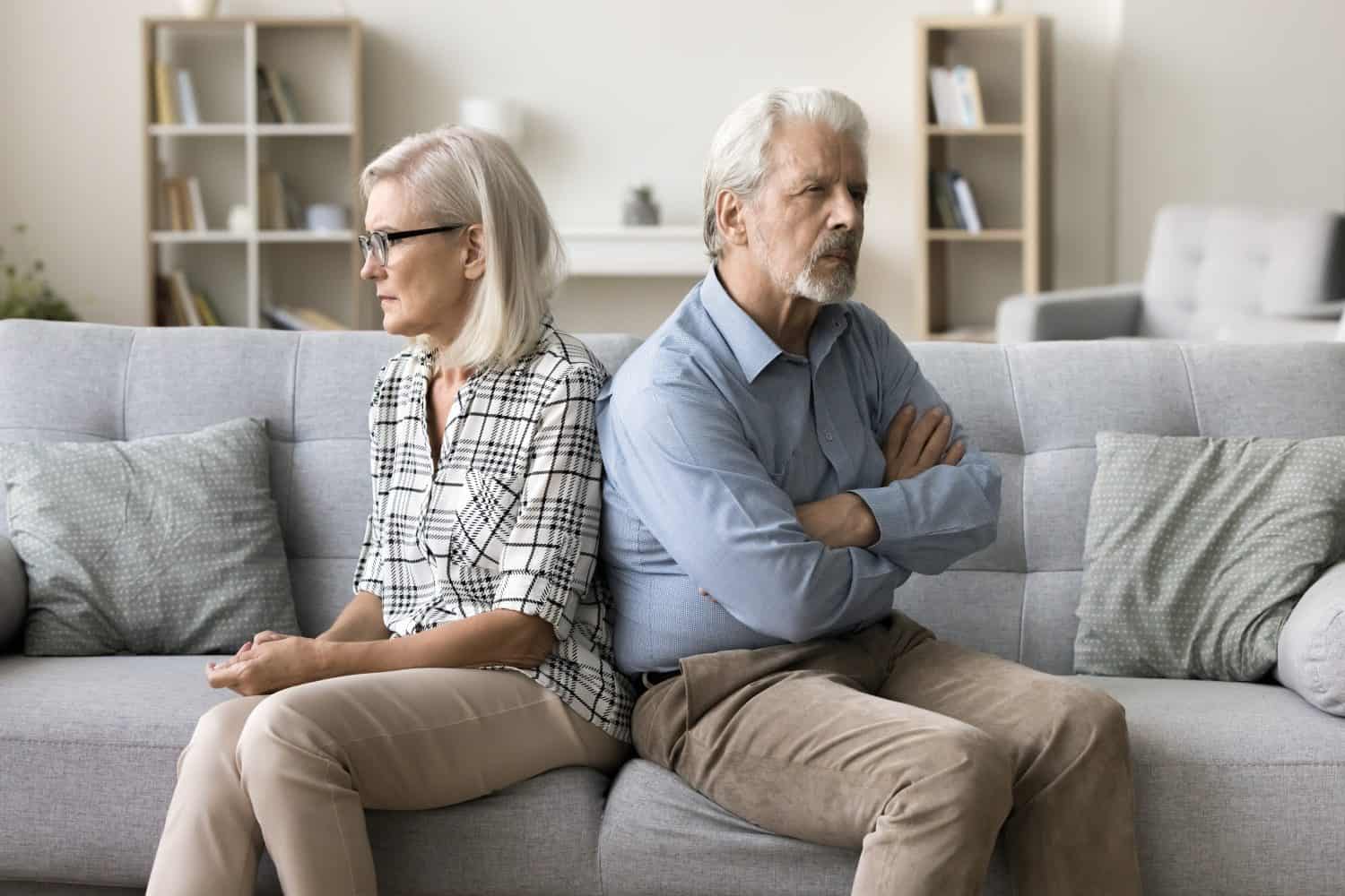 Annoyed ignoring senior couple sitting on home couch back to back, looking away, keeping silence after arguing, thinking on breakup, separation, relationship problems, conflict