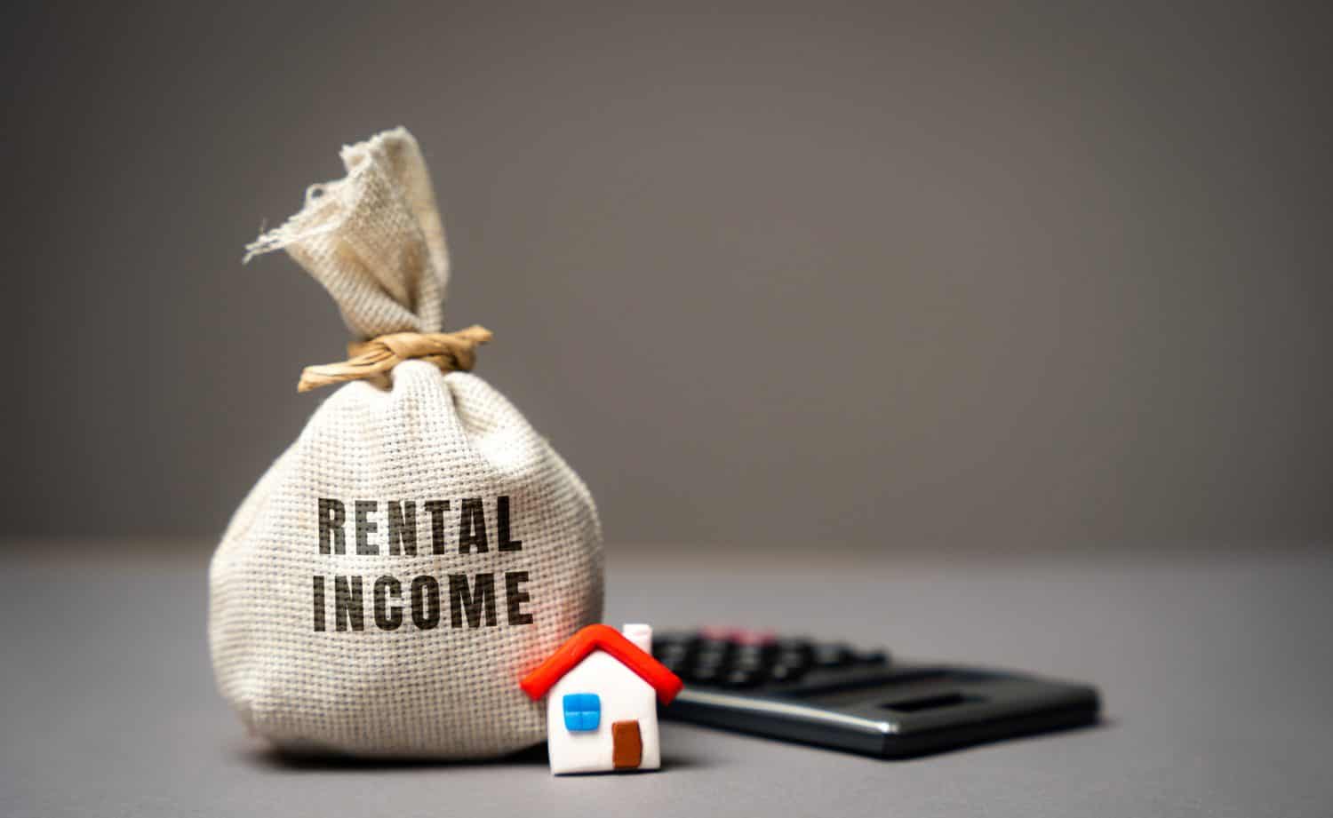 Rental income concept. The concept of profit from the rental of real estate, apartments or houses. Landlord income from housing. Money bag, miniature house and calculator