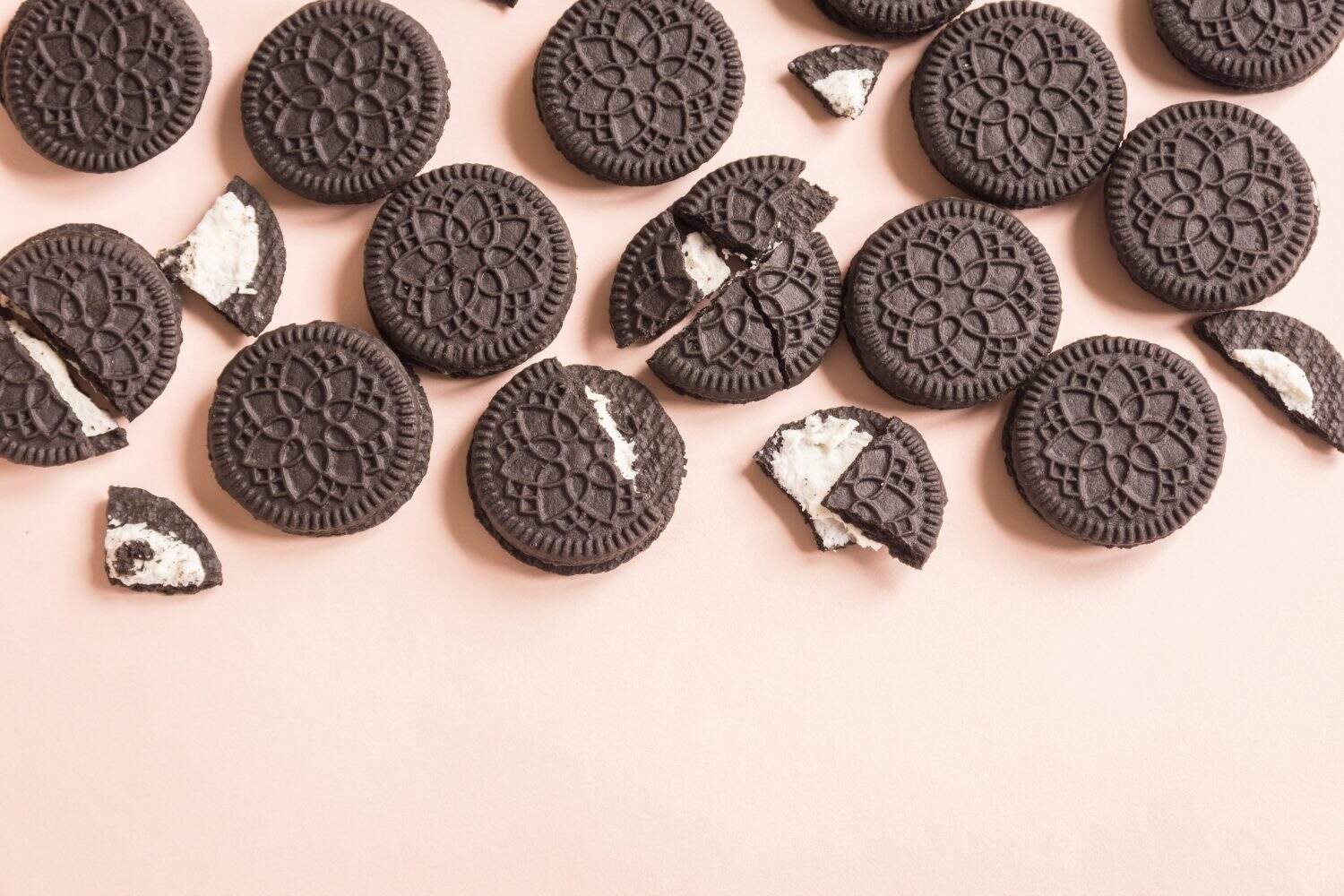 Chocolate and cream sandwich cookies on pink pastel background, top view.