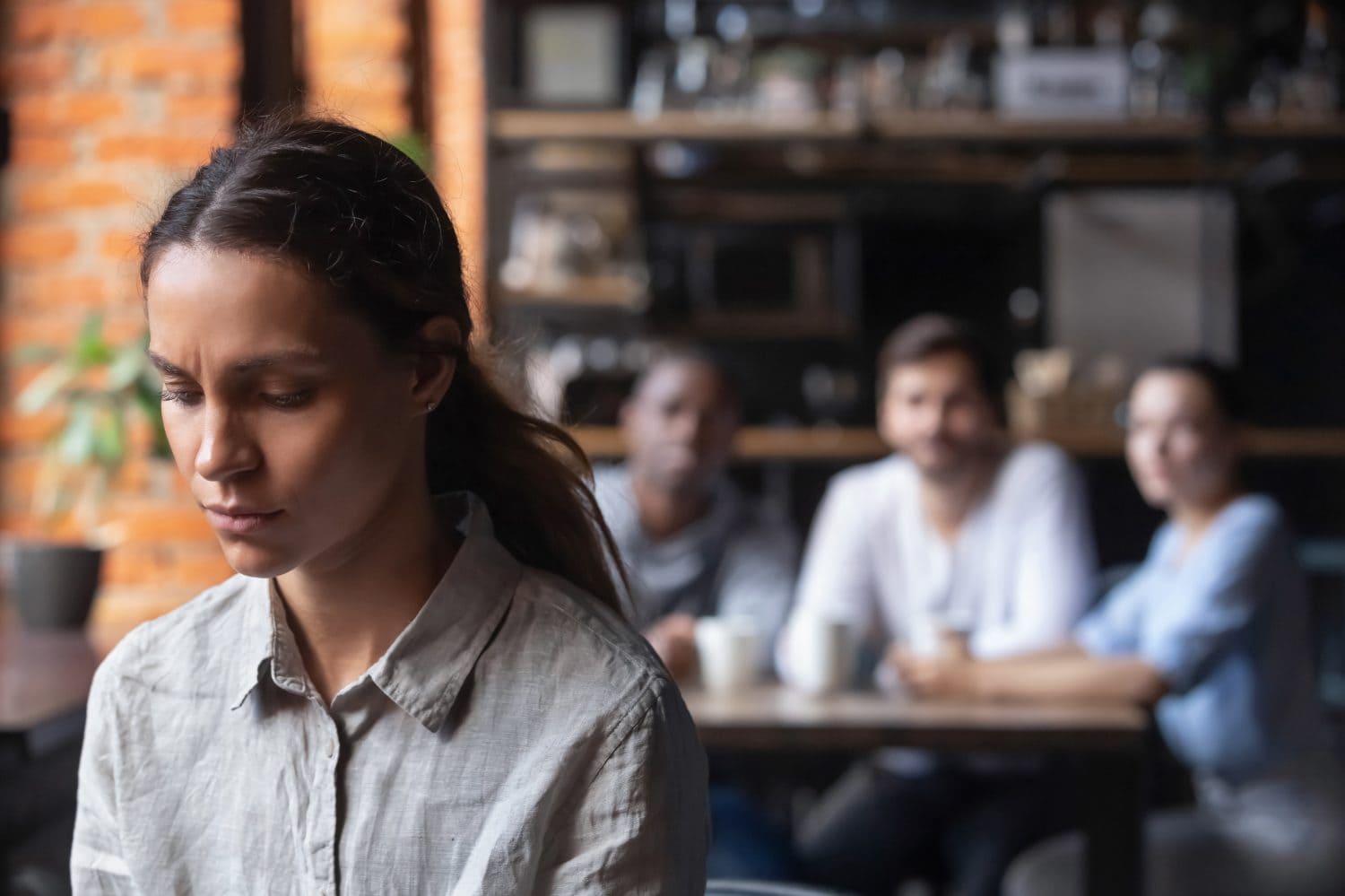 Upset multiracial woman suffering from bullying discrimination excluded girl having problem with bad friends feeling offended and hurt sitting alone in cafe avoiding people social outcast