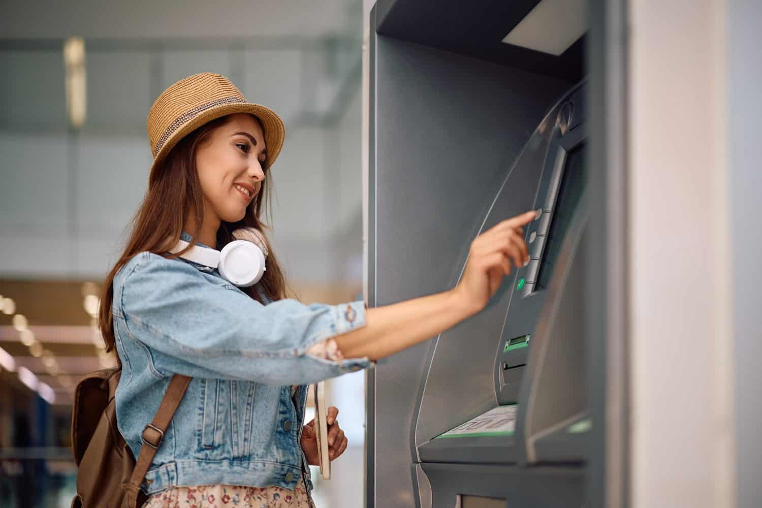 Female tourist withdrawing cash at ATM at the airport. Copy space.