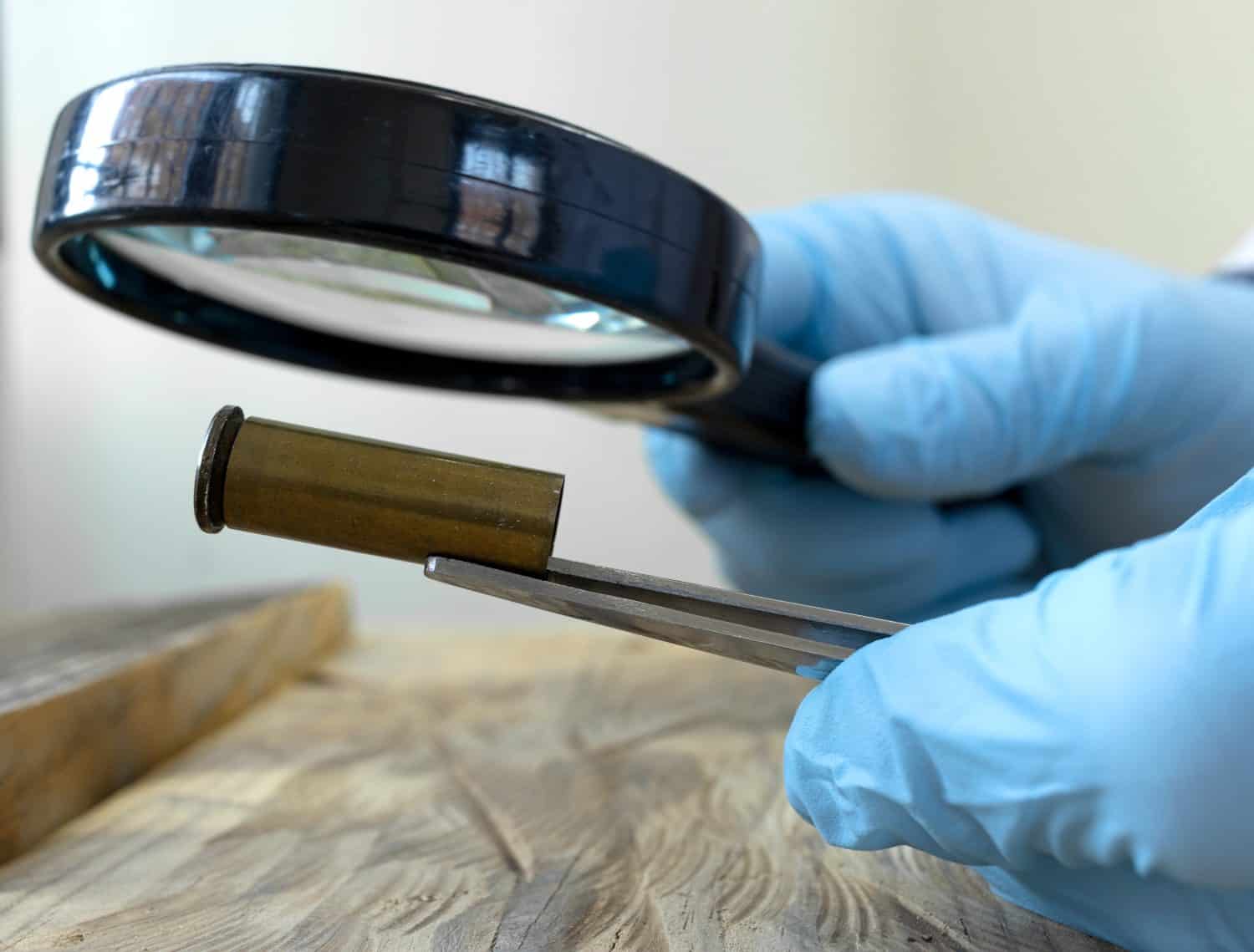 Expert in criminology through magnifying glass examines a bullet case