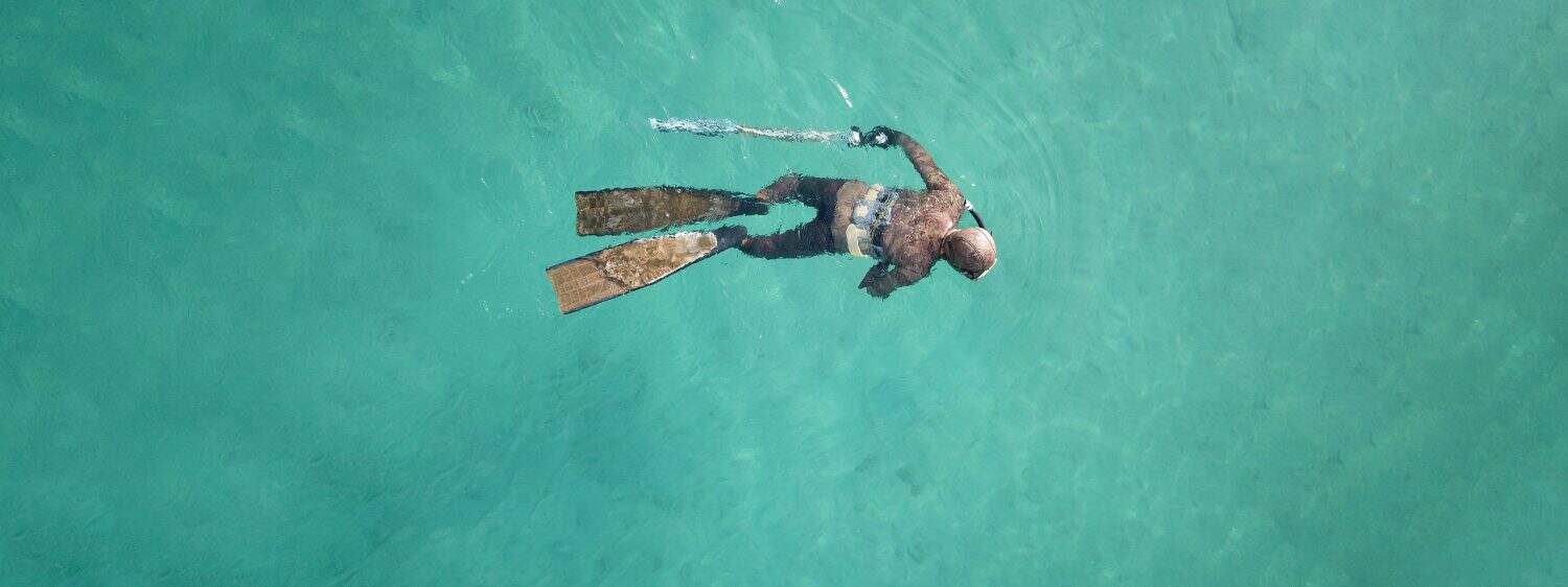 Aerial drone top down ultra wide panoramic photo of spearfishing scuba diver in tropical exotic shallow bay with turquoise clear waters