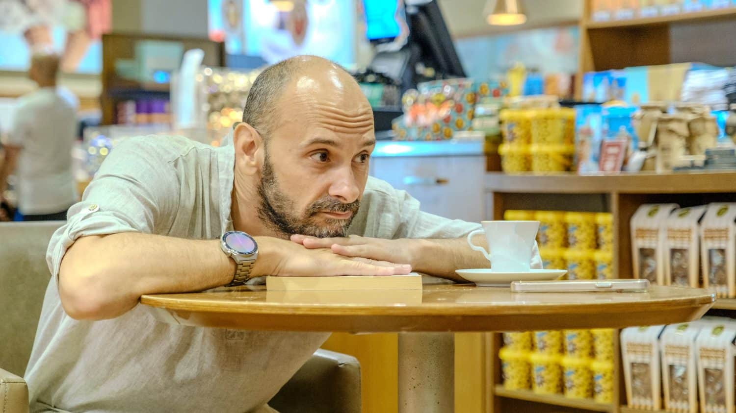 A charismatic middle-aged man wearing a shirt is sitting in a lovely café on a summer evening, enjoying reading a book
