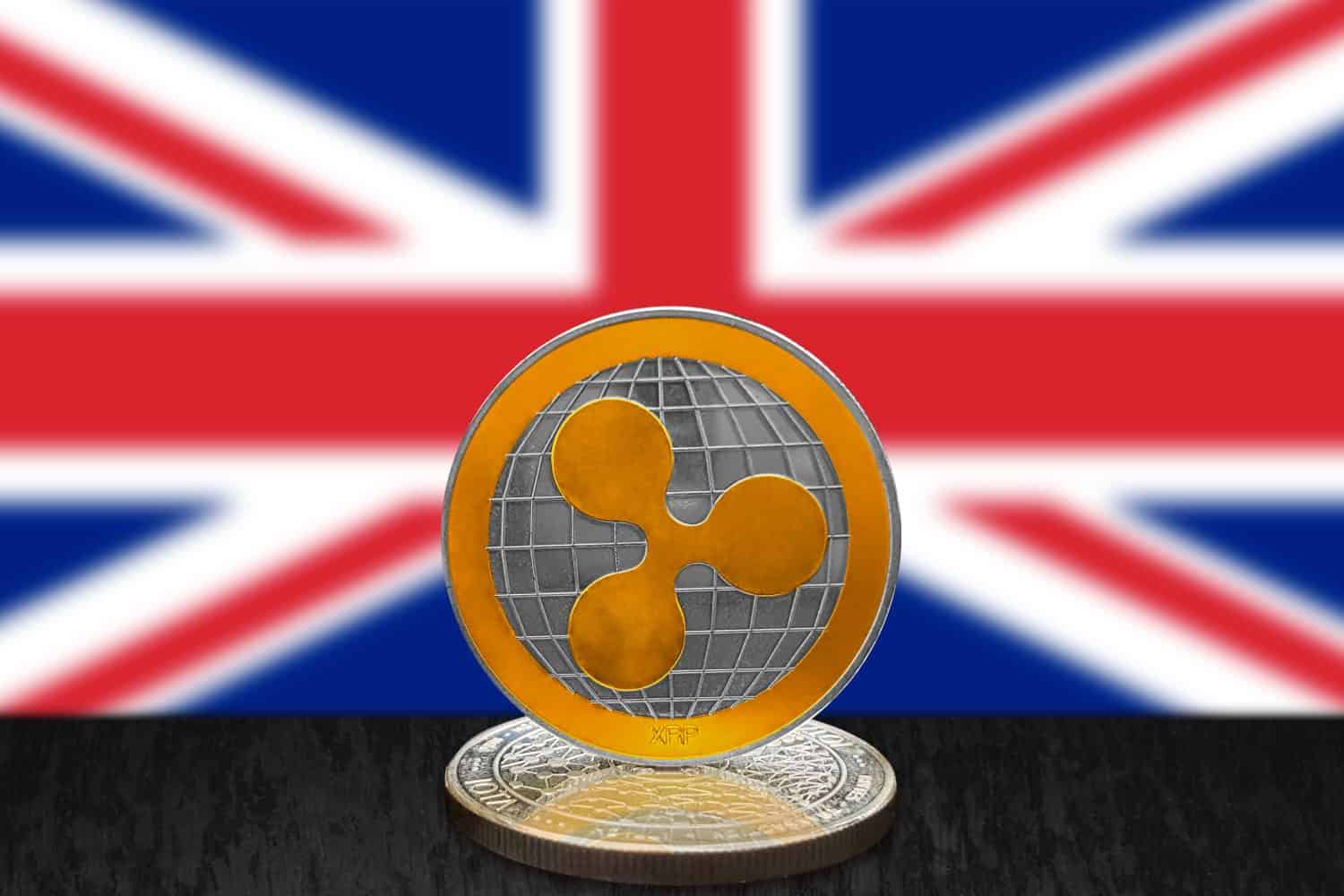 Ripple XRP on cryptocurrency coin with British flag in background. The cryptocurrency coin is golden and in focus. This is a United Kingdom Ripple concept.