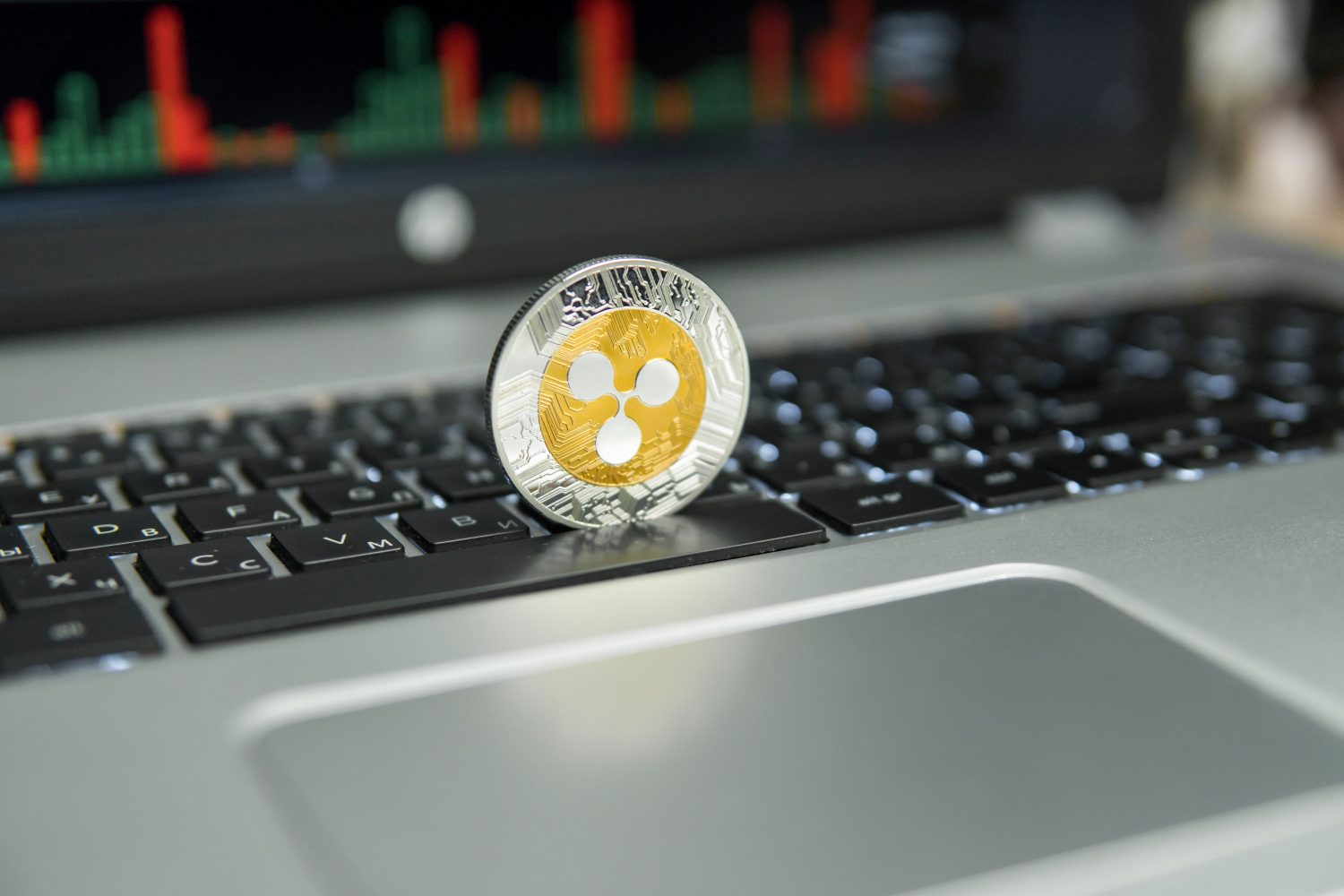 Golden and Silver Ripple coin on a black keyboard of silver laptop and diagram chart graph on a screen as a background. Virtual cryptocurrency concept. Mining of ripples online bussiness. Trading.