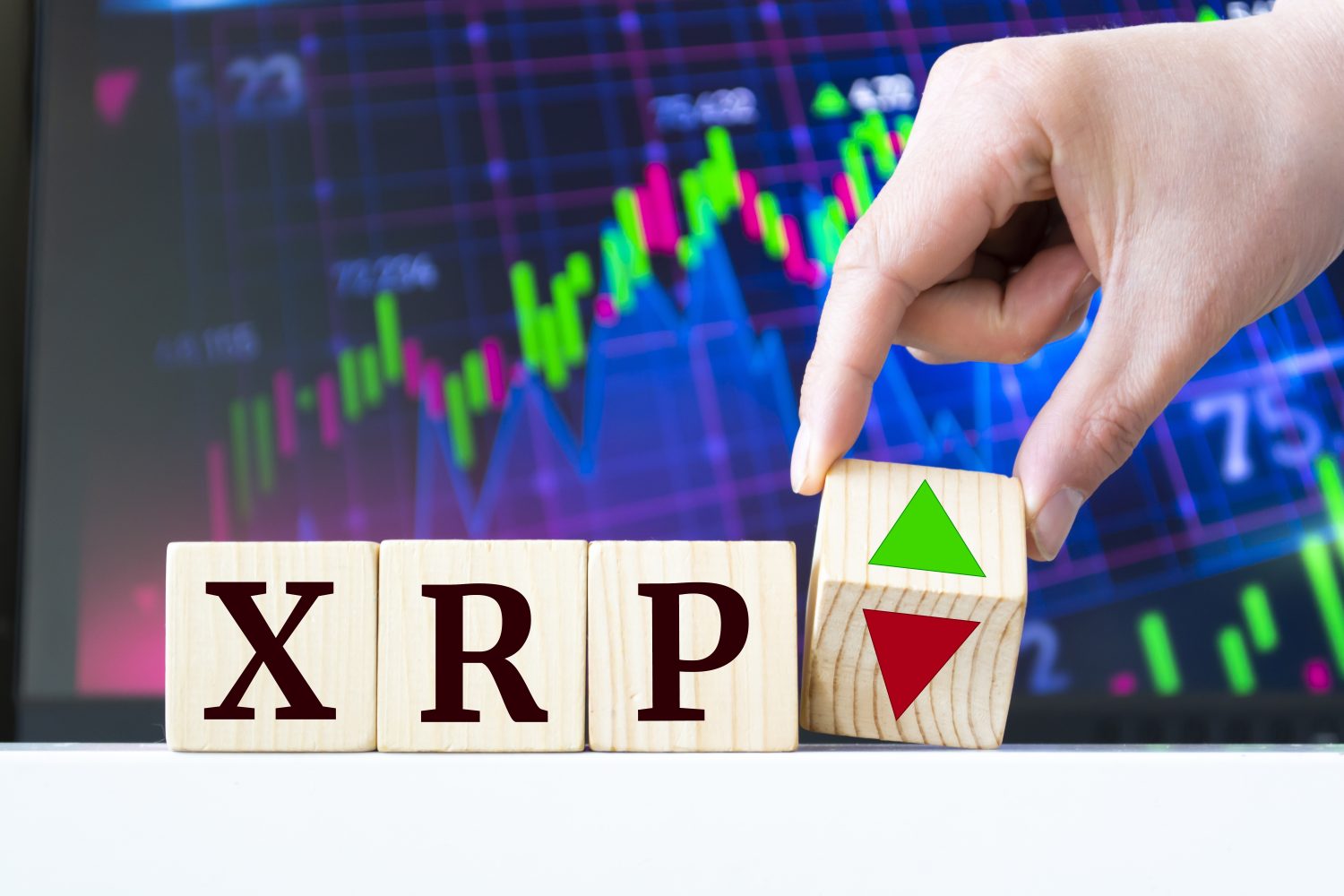 A hand rotates a wooden cube to indicate the fall or rise of the cryptocurrency Ripple XRP
