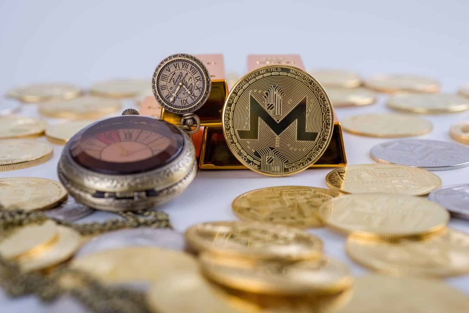 Cryptocurrency concept. Shining Monero cryptocurrency coin in front of five gold bars and by an old vintage pocket watch, isolated in white background. selective focus.